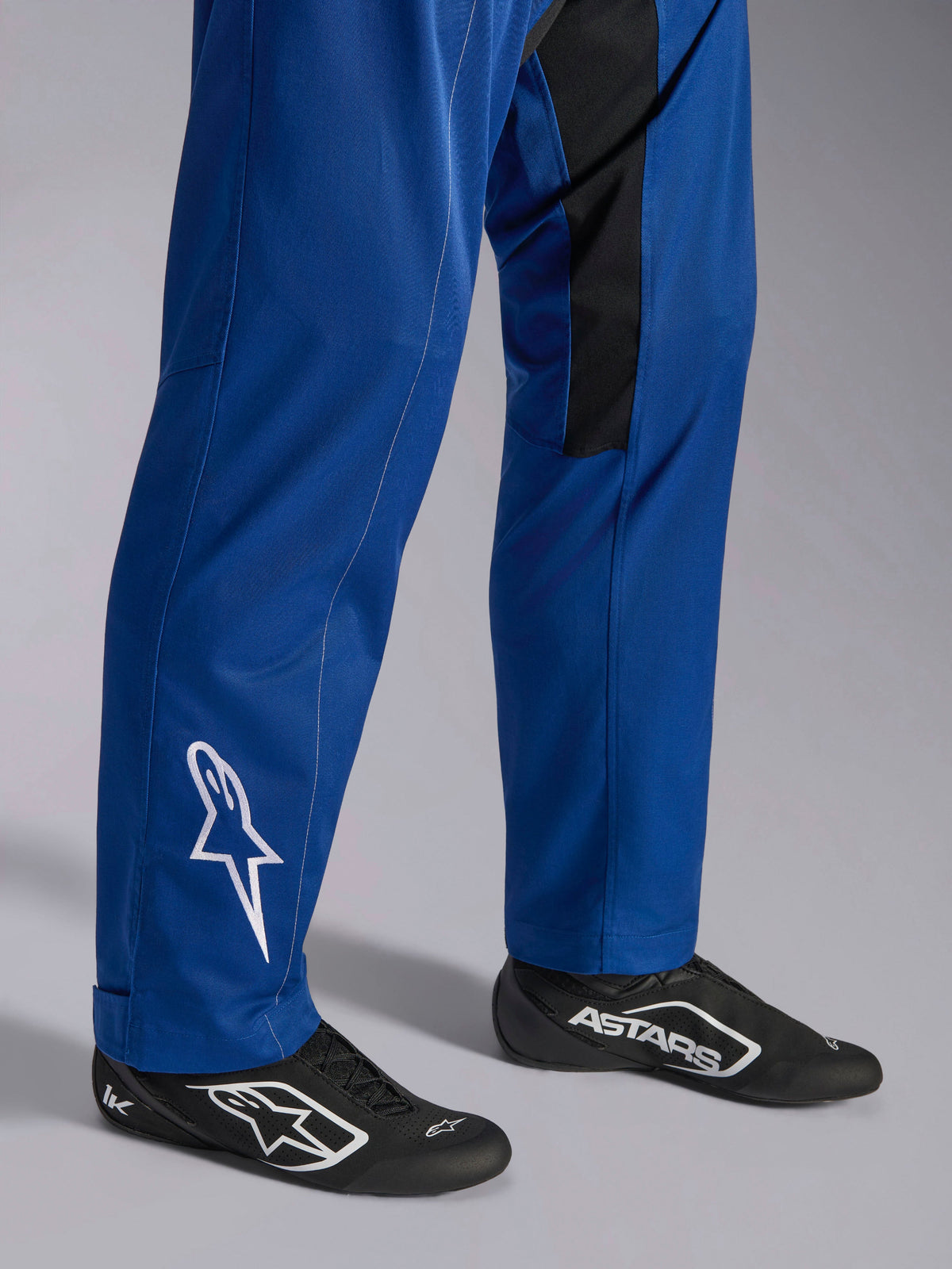 Alpinestars Kart Indoor V2 Anzug, Blau, Nahaufnahme der Unterschenkel und Füße mit weißem Stern-Logo am Knöchel, verstellbare Beinabschlüsse und schwarze Rennschuhe, strapazierfähige Kartbekleidung für den Freizeiteinsatz auf der Rennstrecke