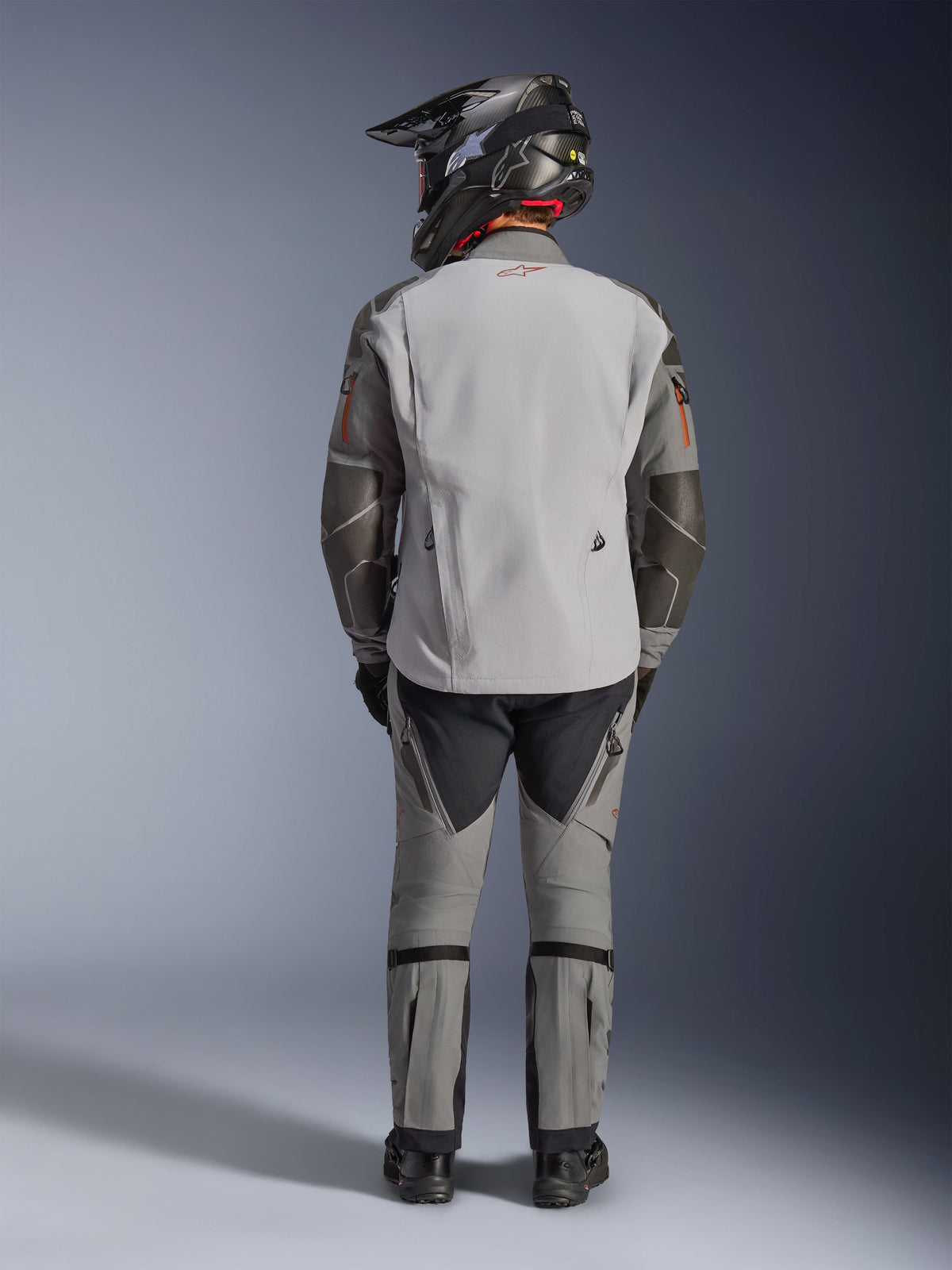 Alpinestars Nazca 3L GORE-TEX PRO Jacket, Adventure Motorcycle Jacket, Dark Gray and Mid Gray, rear view of rider wearing complete gear, worn with matching pants and black adventure helmet, featuring a red logo on the back and Superfabric reinforcements on the elbows, durable textile design for adventure touring.