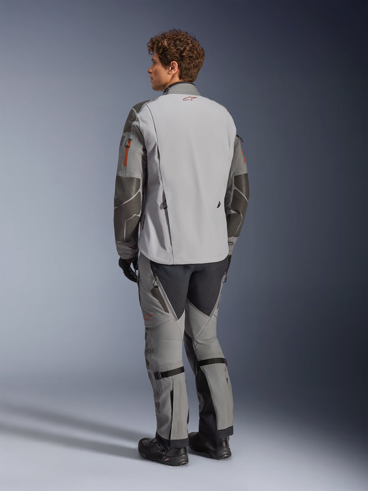 Alpinestars Nazca 3L GORE-TEX PRO Jacket, Adventure Motorcycle Jacket, Dark Gray and Mid Gray, rear view worn with matching adventure pants and black boots, featuring dark gray Superfabric reinforcements on the sleeves, orange zipper accents, and a small red logo on the back collar.