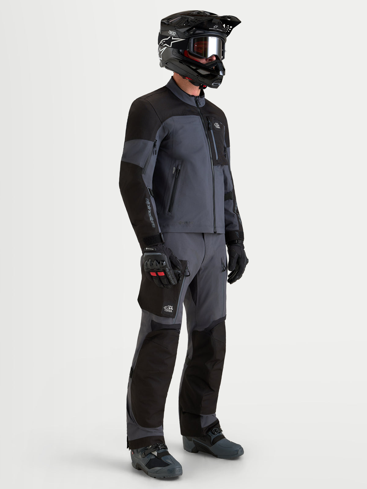 Alpinestars Arenis Gore-Tex Gear Set, heren adventure motorjas en motorbroek in zwart en donkergrijs, zijaanzicht op een model met bijpassende uitrusting en helm, waterdichte all-terrain motorkleding
