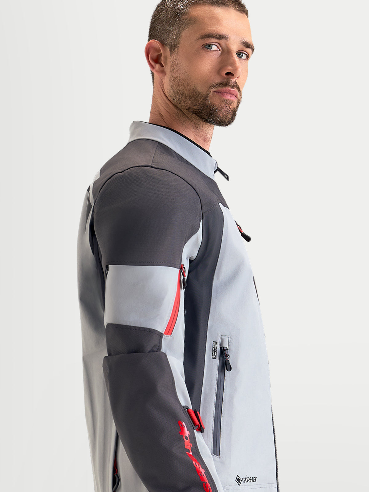Alpinestars Arenis Gore-Tex jas, heren adventure-motorjas in middenrijs, donkergrijs en zwart, zijaanzicht op model met waterdichte textielconstructie en ergonomische kraag