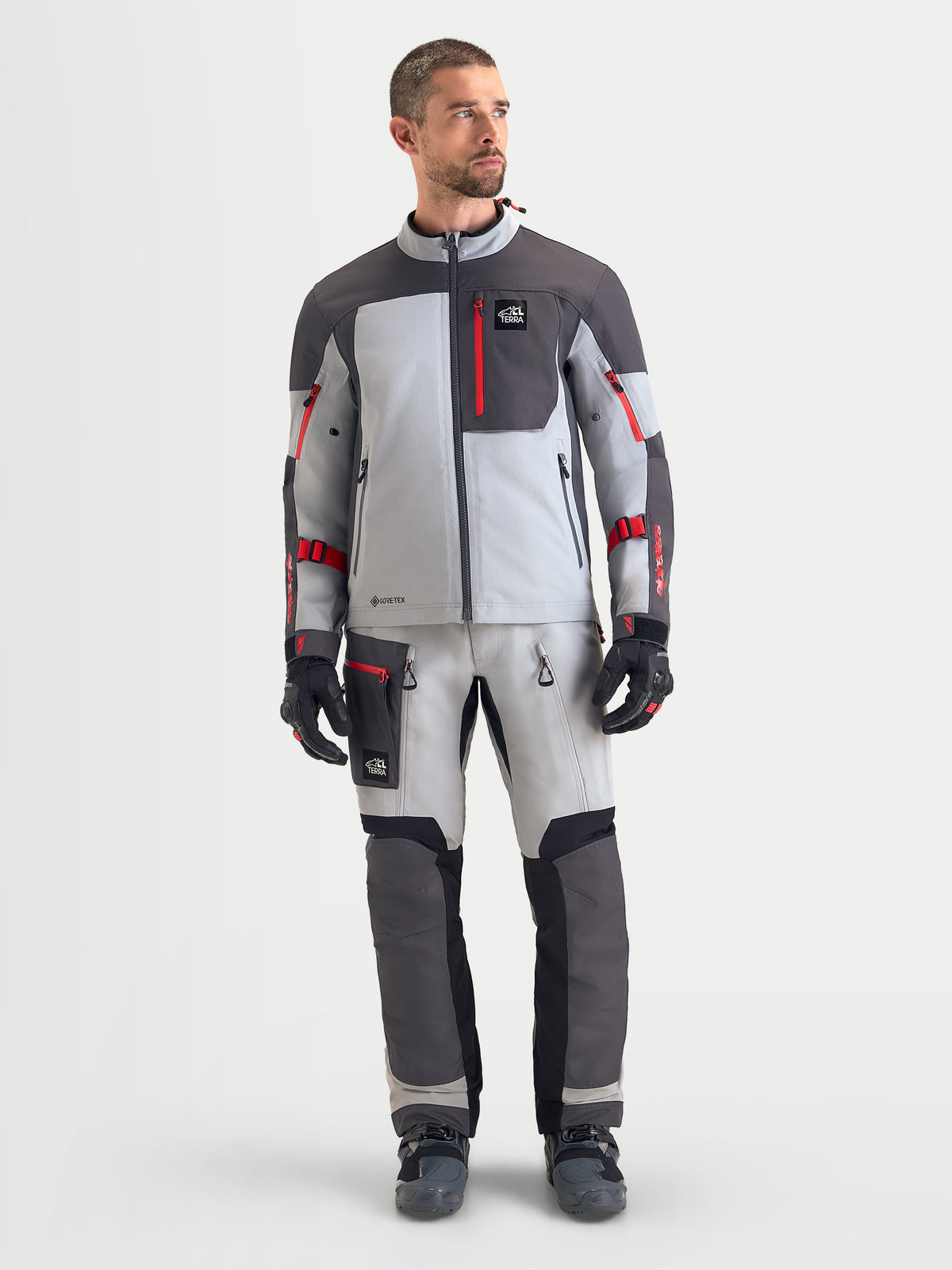 Alpinestars Arenis Gore-Tex jas, heren adventure touring motorjas in middengrijs, donkergrijs en zwart, studioschot aan de voorkant met waterdichte textielconstructie en rode ritssluitingsdetails
