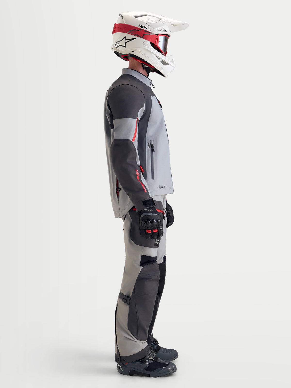 Alpinestars Arenis Gore-Tex jas, heren adventure motorjas in middengrijs, donkergrijs en zwart, zijaanzicht van een rijder met de waterdichte textieljas, bijpassende uitrusting en een wit-rode helm
