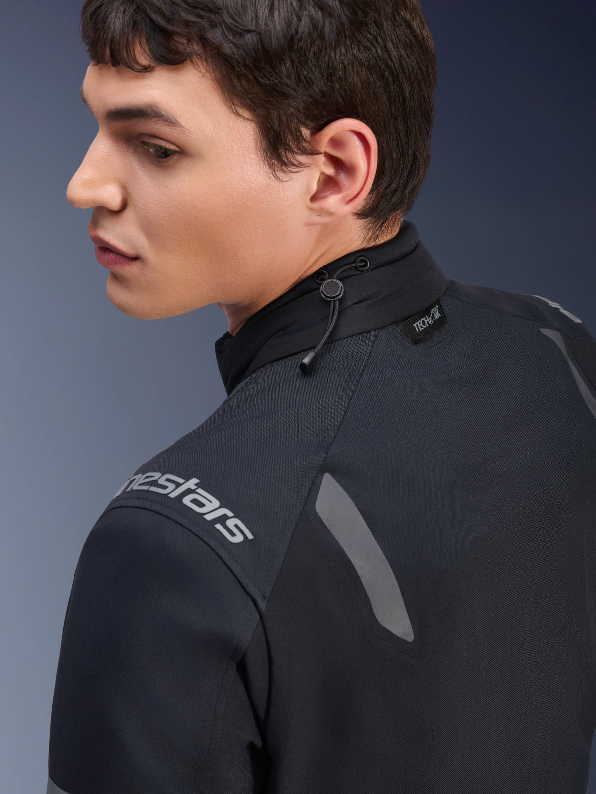 Alpinestars ST-7 2L GORE-TEX Jacke, Motorradjacke in Schwarz und Dunkelgrau, Nahaufnahme des Kragens mit Kordelzugverstellung und Tech-Air-Label, mit grauen reflektierenden Akzenten und Markenlogo auf der Schulter.