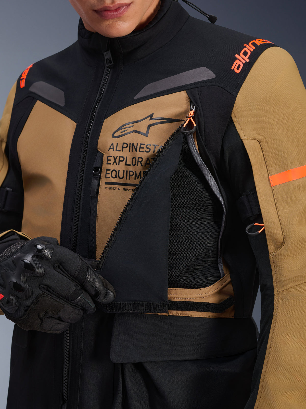 Alpinestars ST-7 2L GORE-TEX jas, adventure touring motorjas, Gobi bruin en zwart, close-up van het open ventilatiepaneel op de borst met ademend mesh, voorzien van Alpinestars Exploration Equipment-branding en oranje accenten.
