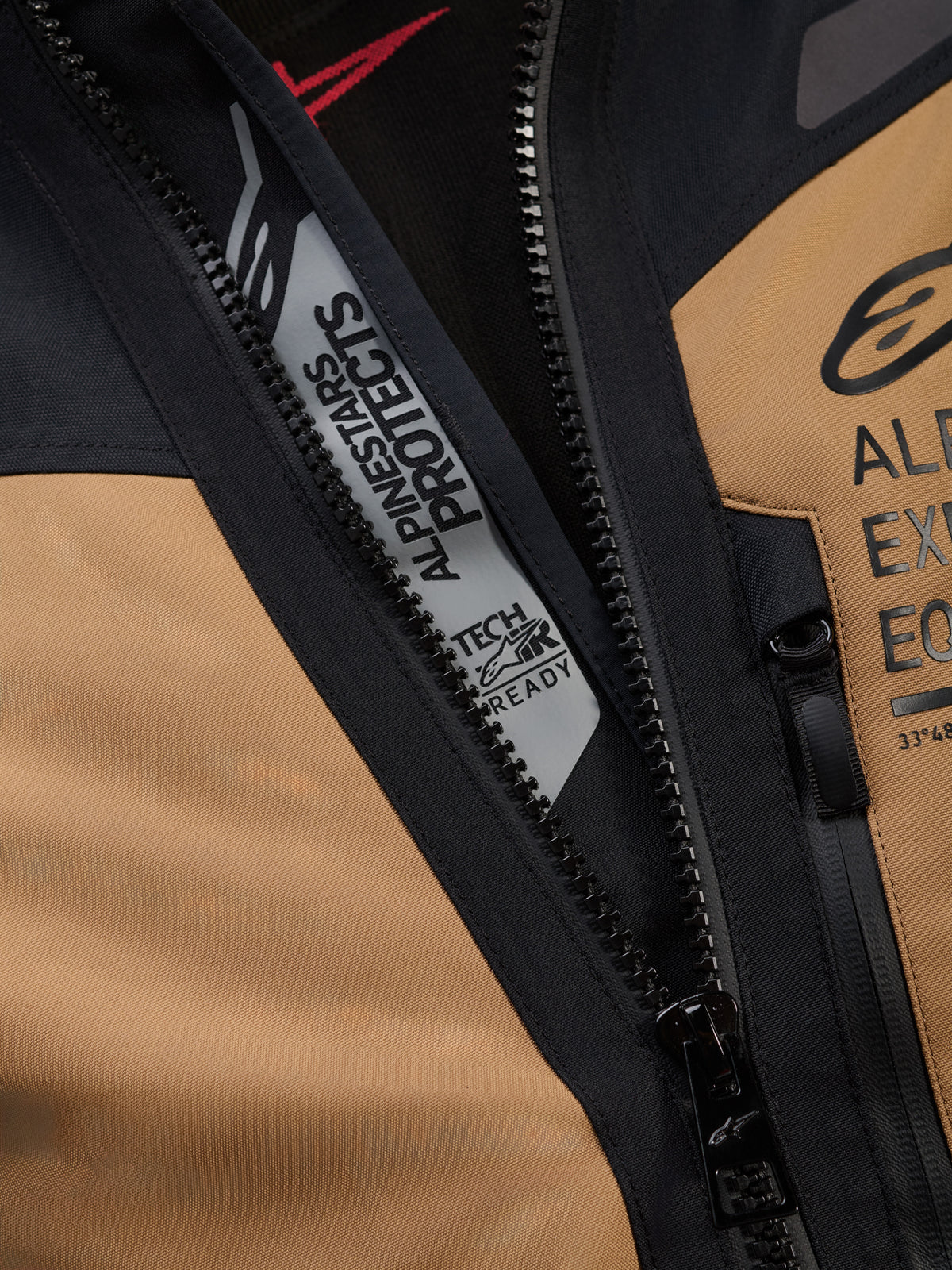 Close-up detail van de Alpinestars ST-7 2L GORE-TEX jas in Gobi Brown en zwart, met 'ALPINESTARS PROTECTS' en 'TECH-AIR READY' branding aan de binnenzijde van de hoofdrits, robuuste textielconstructie en borstlogo's
