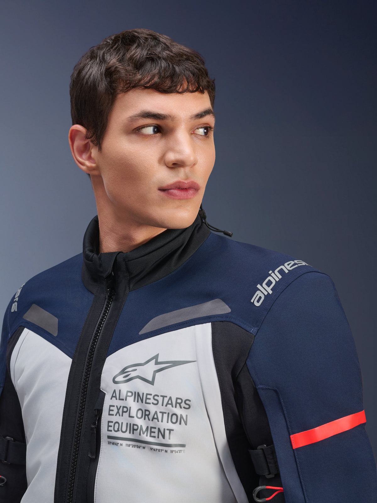 Alpinestars ST-7 2L GORE-TEX jas, Ice Gray, donkerblauw en zwart, gedragen door mannelijk model, voorzien van Alpinestars Exploration Equipment-branding op de borst, hoge kraag en rood accent op de mouw, duurzaam textielontwerp voor adventure touring