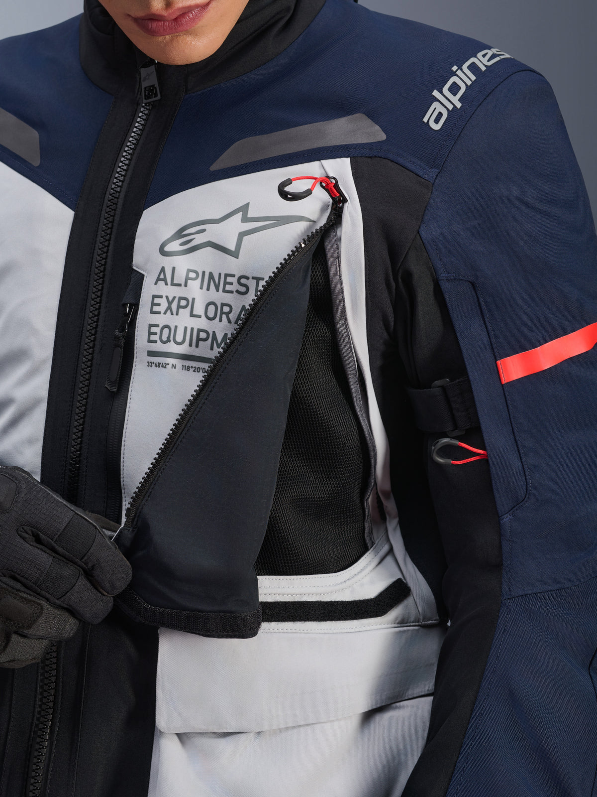 Alpinestars ST-7 2L GORE-TEX Jas, Adventure Touring Jas, Ice Gray, donkerblauw en zwart, detailopname van het geopende ventilatiepaneel op de borst waarbij zwart mesh zichtbaar is, met het Alpinestars Exploration Equipment-logo en rode accent trekkoorden