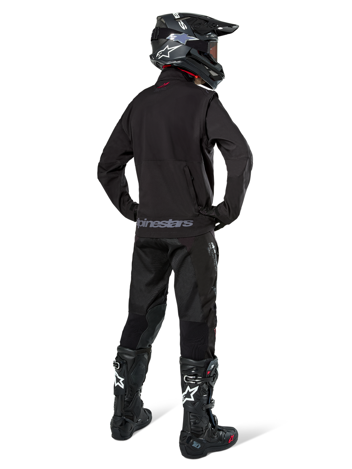 Enduro-Fahrer in der Rückansicht, trägt die Alpinestars Lite-Dura Softshell-Jacke in Schwarz, kombiniert mit einer schwarzen technischen Fahrhose und Stiefeln, mit einer Reißverschlusstasche am Rücken und dem Alpinestars-Logo am unteren Saum, komplette Offroad-Ausrüstung für Motocross.