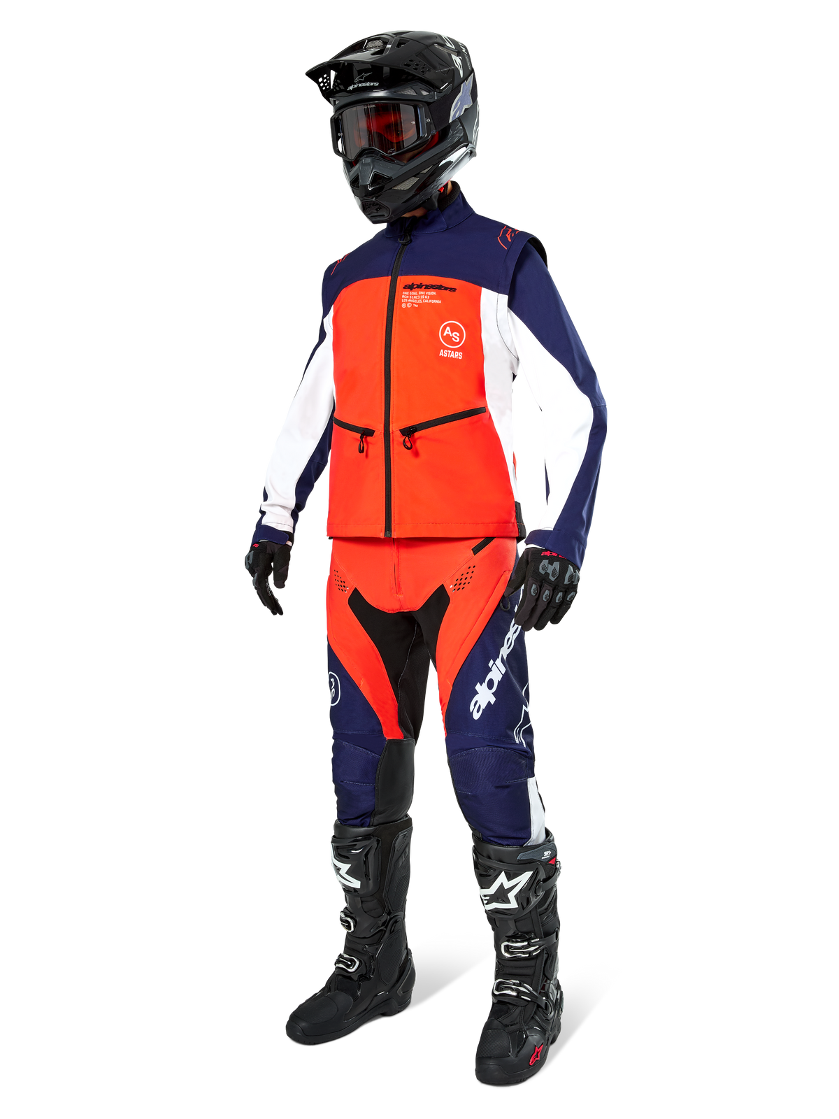 Motocross-Fahrer in der Alpinestars Lite-Dura Softshell-Jacke in Navy, Hot Orange und Weiß, komplett mit passender Offroad-Hose, schwarzem Helm mit Goggles und schwarzen Rennstiefeln, abgestimmtes Enduro-Ausrüstungsset
