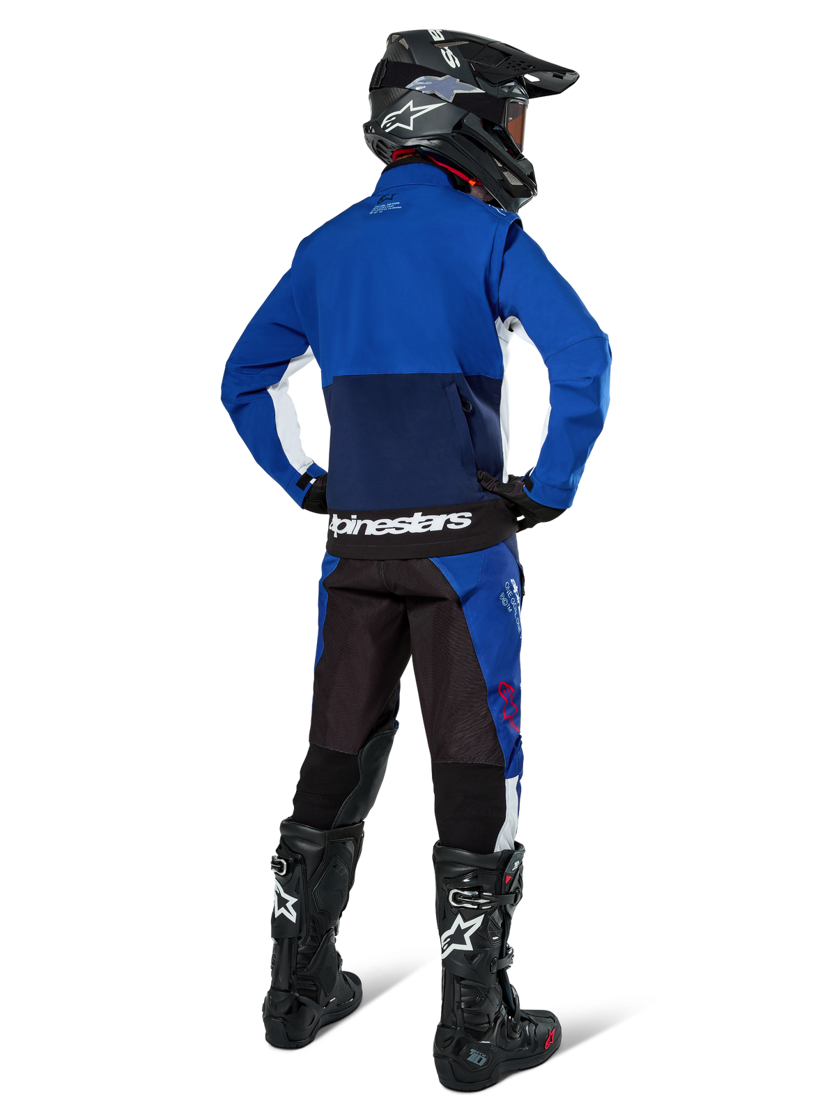 Motocross-Fahrer von hinten in der Alpinestars Lite-Dura Softshell-Jacke in Navy Bright Blue und Weiß, kombiniert mit passender Enduro-Hose, schwarzem Helm und schwarzen Stiefeln, komplette Offroad-Rennausrüstung