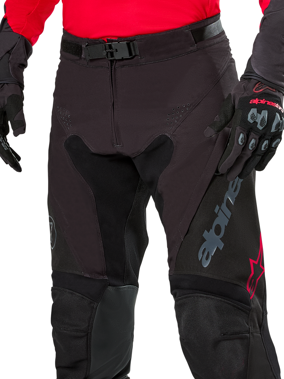 Gros plan sur le pantalon d'enduro Alpinestars Pro-Dura, coloris Noir Magnet Blanc avec des accents rouges, doté d'une fermeture par boucle magnétique sécurisée et d'une braguette zippée, porté avec un maillot rouge et des gants noirs assortis, construction en ripstop durable pour la conduite tout-terrain