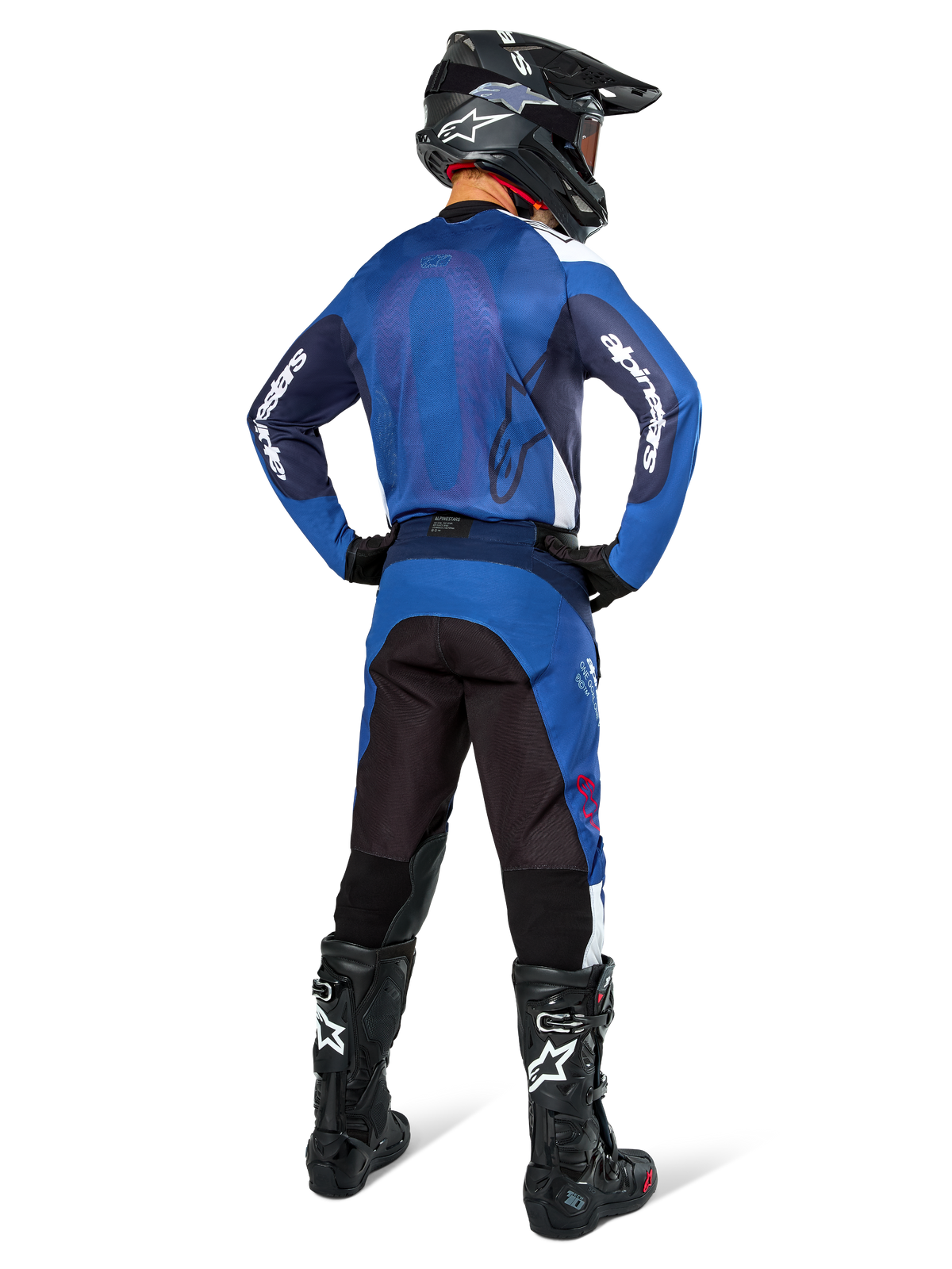 Pantalon Alpinestars Pro-Dura, pantalon de motocross et d'enduro, bleu marine, bleu vif et blanc, vue de dos, porté avec un maillot bleu assorti, un casque noir et des bottes Tech noires, construction durable avec inserts extensibles pour la conduite tout-terrain