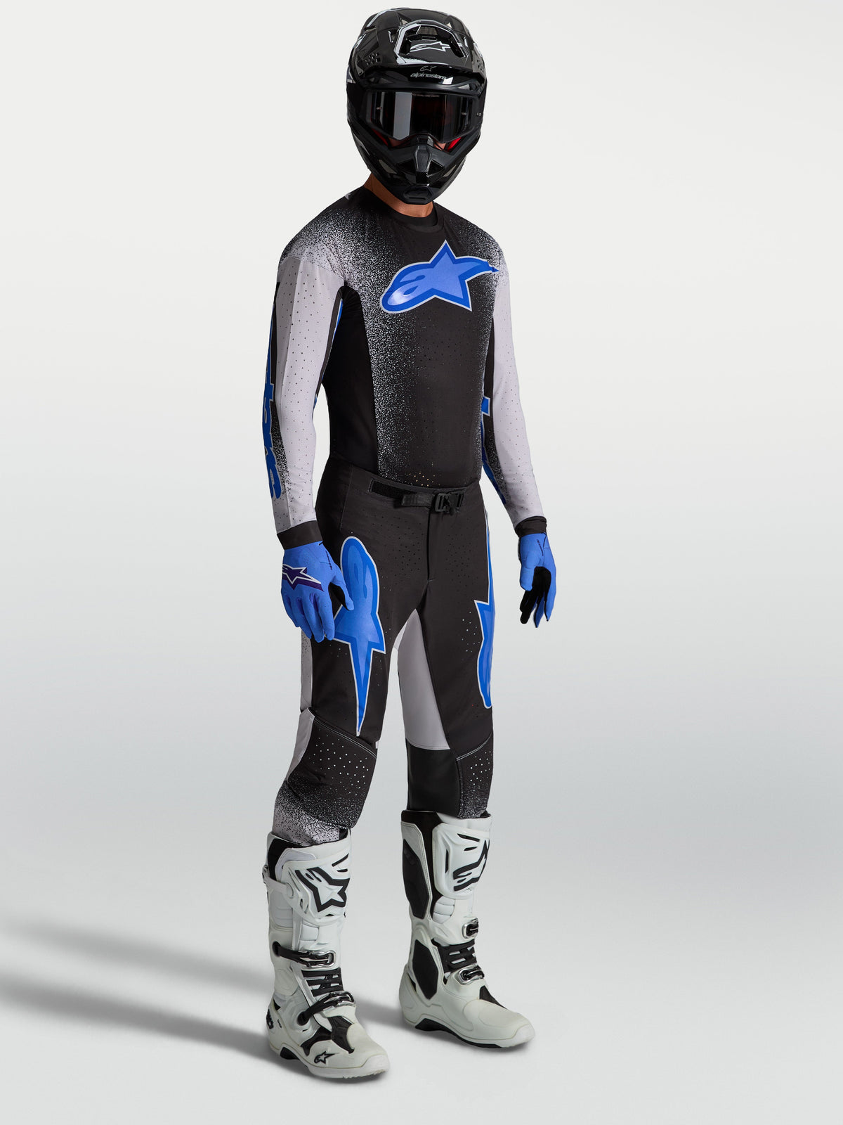 Alpinestars Supertech Hiten AFD-broek, motocrossuitrusting voor heren in zwart en blauw, op model met bijpassende jersey en witte motorlaarzen, professionele off-road raceprestaties.