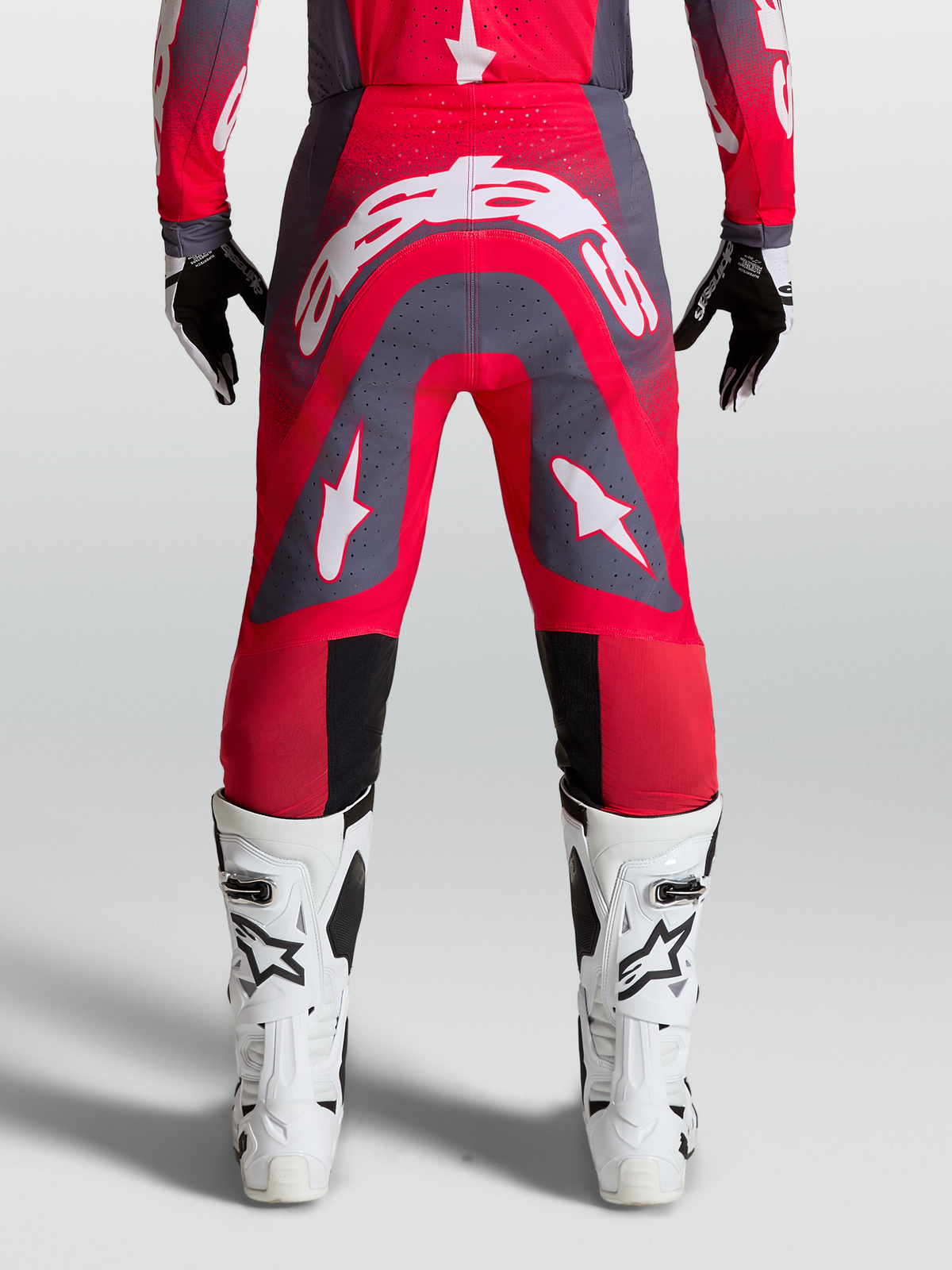 Alpinestars Supertech Hiten AFD Broek, professionele motocrossbroek, rood en grijs met witte logo's, gedragen met witte laarzen.