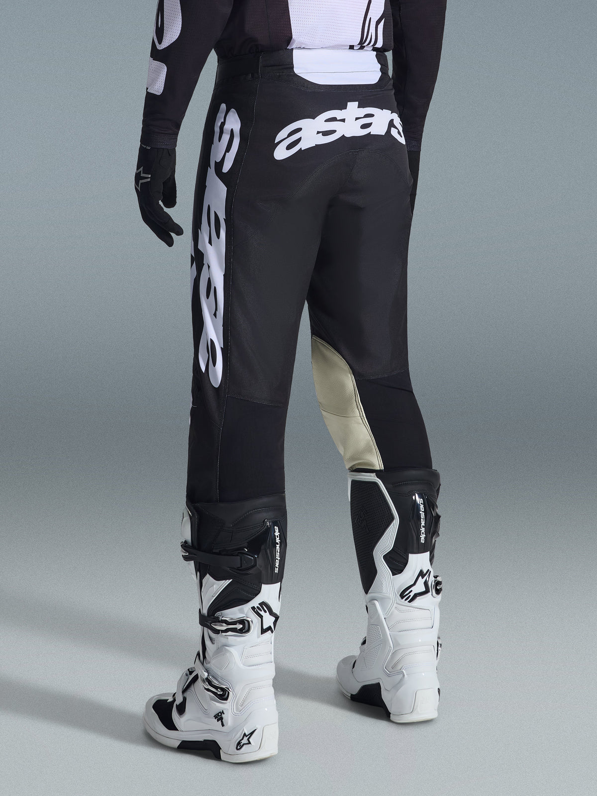 Rückansicht der Alpinestars 2026 Racer Air Riway Hose in Schwarz und Weiß, mit markantem weißem „astars“-Branding auf dem Gesäß und am Bein sowie cremefarbenen Leder-Innenpaneelen an den Knien, kombiniert mit passenden schwarz-weißen Motocross-Stiefeln und Trikot.