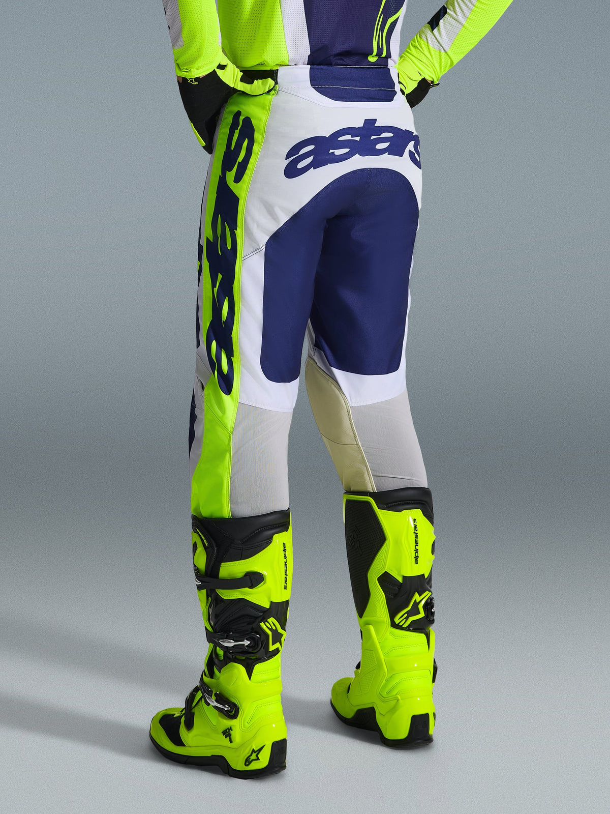 Alpinestars 2026 Racer Air Riway Hose, Motocross-Hose, Hellgrau, Gelb Fluo und Blau, Rückansicht mit „astars“-Logo auf dem Gesäß und der Seite, getragen mit passenden fluorgelben Motocross-Stiefeln, sportliche Rennpassform für Offroad-Performance.