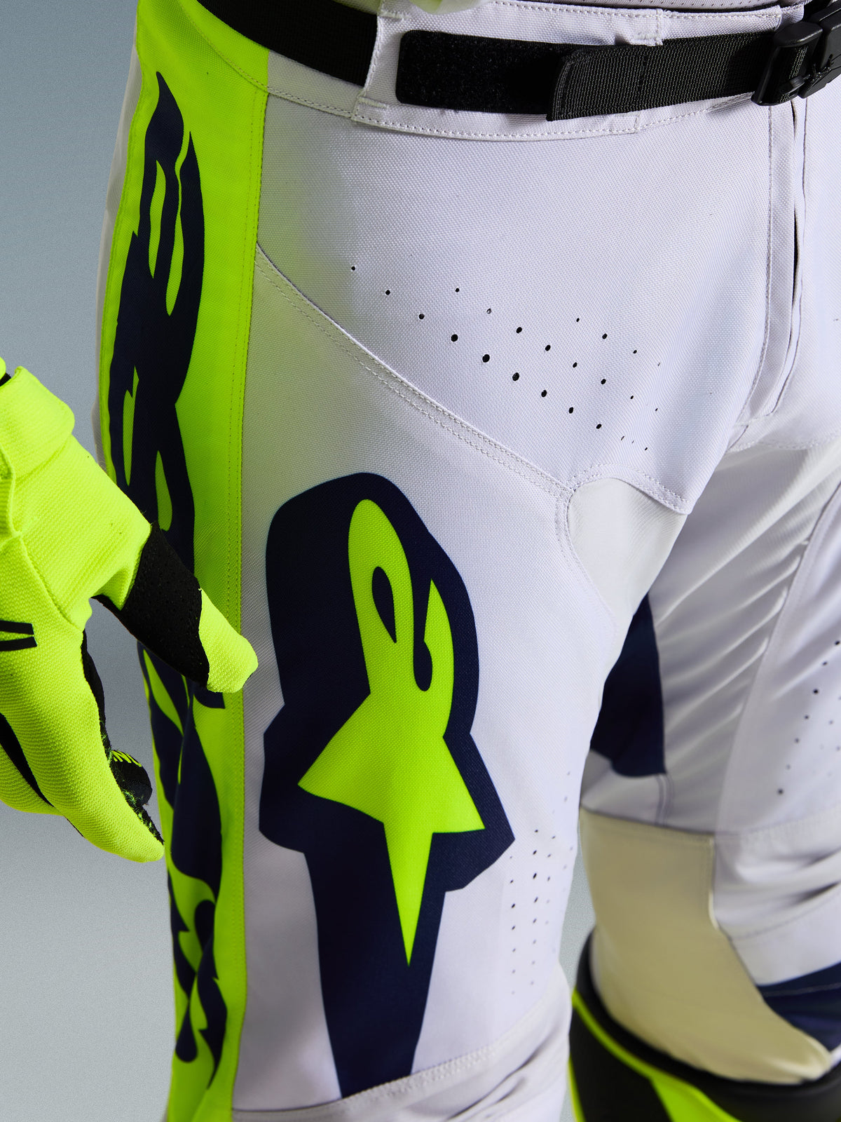 Alpinestars 2026 Racer Air Riway Hose, Nahaufnahme einer weiß-marineblauen Motocross-Hose mit leuchtend gelben Einsätzen, lasergeschnittene Belüftungsöffnungen für die Luftzirkulation, markantes Astar-Branding, kombiniert mit einem passenden gelben Handschuh
