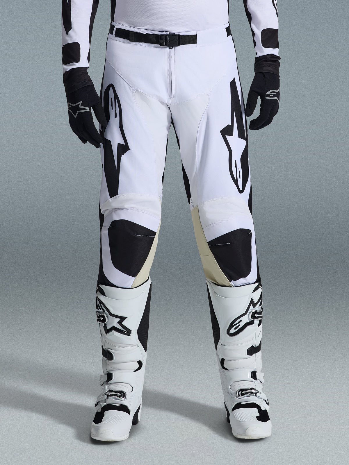 Alpinestars 2026 Racer Riway broek, motorcrossbroek, wit en zwart, gedragen met bijpassende wit-zwarte motorcrosslaarzen en zwarte handschoenen, voorzien van opvallende zwarte Alpinestars-branding op de dijen, technisch ontwerp voor off-road prestaties.