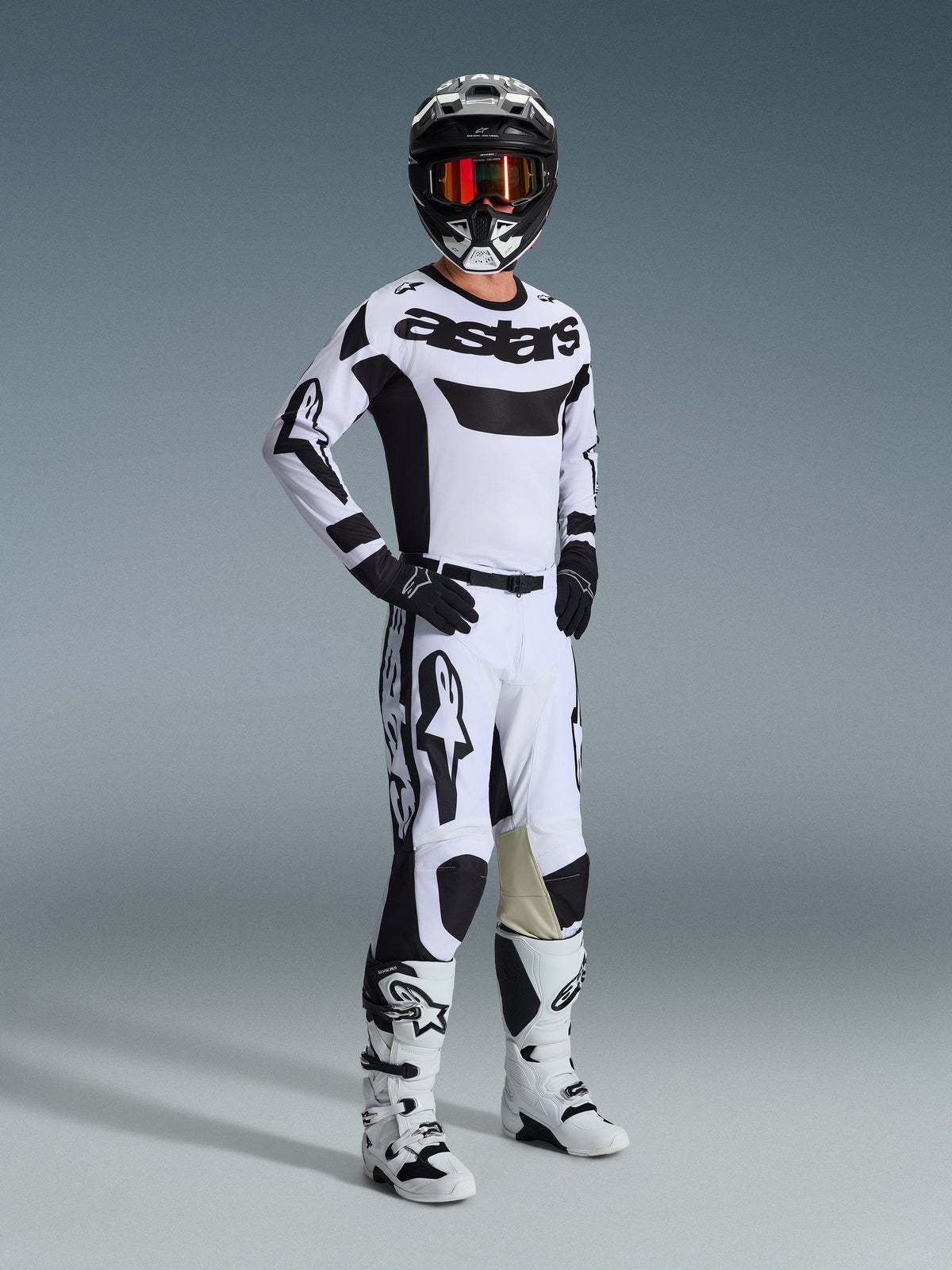 Alpinestars 2026 Racer Riway Broek, motorcrossbroek, wit en zwart, gedragen als onderdeel van een complete race-uitrusting met bijpassend shirt, laarzen en helm, met opvallende zwarte branding en geitenleren panelen aan de binnenzijde van de knie, professionele off-road racekit