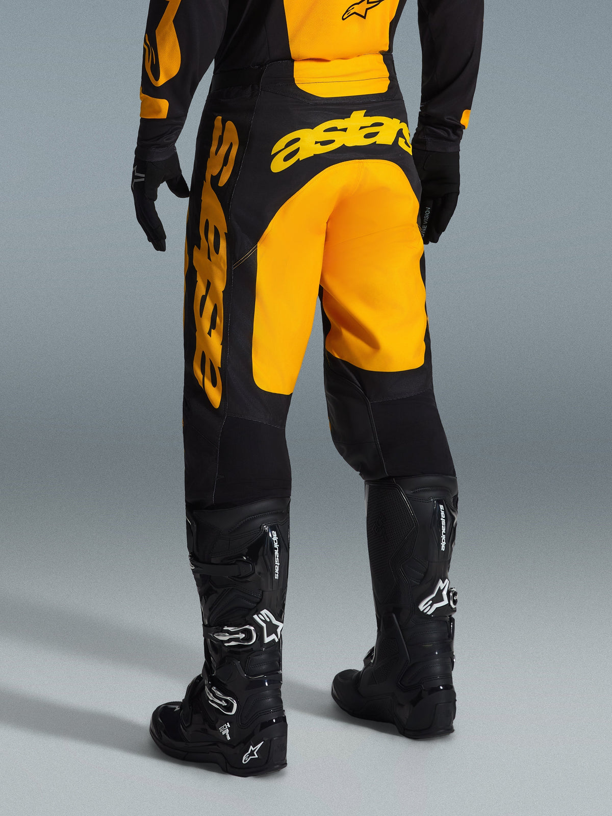 Alpinestars 2026 Racer Riway Pants, pantalon de motocross, jaune et noir, vue arrière montrant le marquage Astars jaune imposant sur l'assise et la jambe, associé à des bottes et gants de motocross noirs