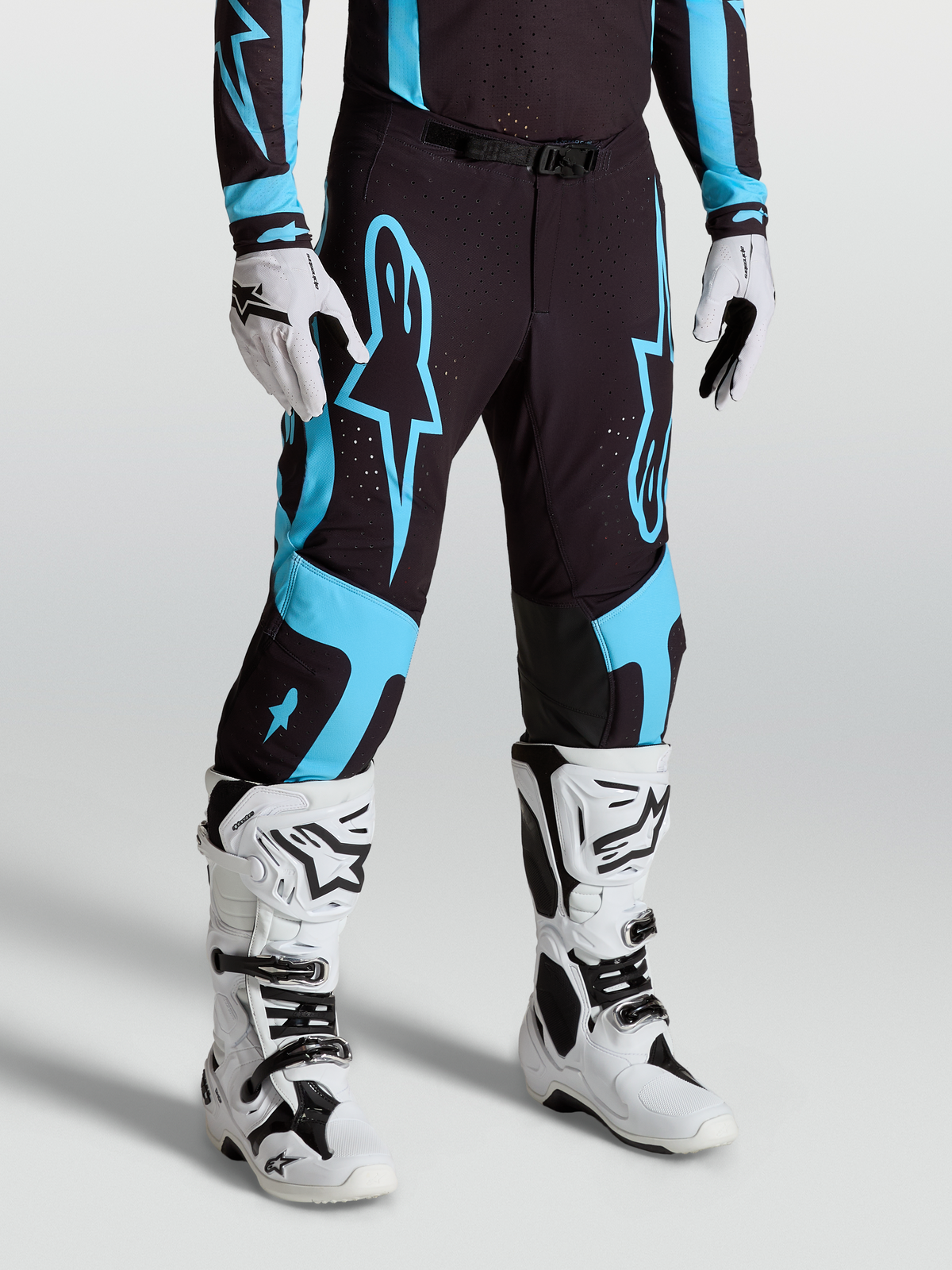 Alpinestars Supertech Vesta Hose, Motocross-Rennsport-Hose für Herren, Schwarz und Türkis, aus Stretch-Ripstop mit Innenkniepanels aus Ziegenleder, getragen mit weißen Tech 10 Stiefeln und Handschuhen.