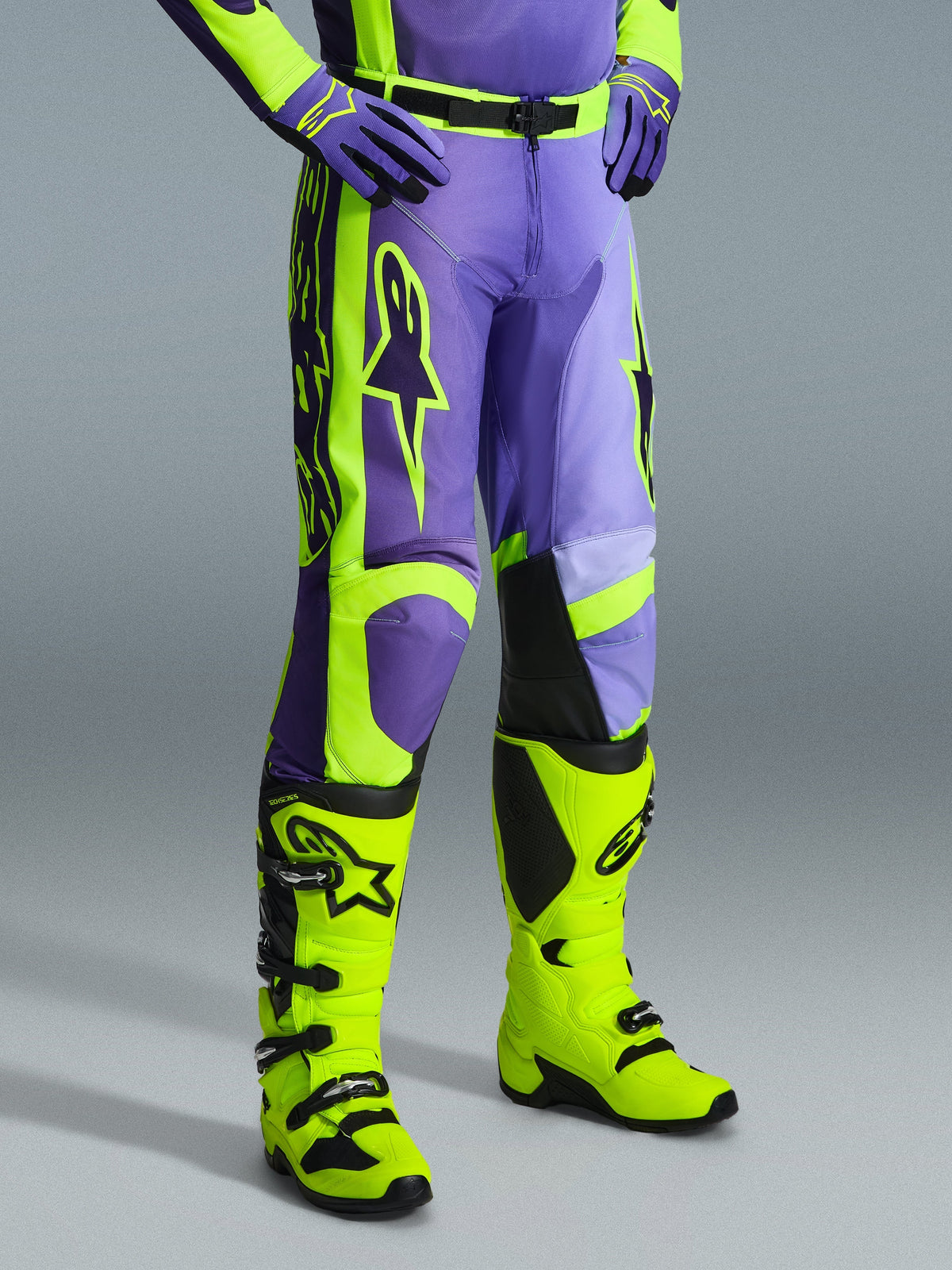 Pantalon Alpinestars Racer Portl 2026, pantalon de motocross violet et jaune fluo, porté par un pilote avec des bottes jaune fluo assorties et des gants violets, arborant le logo Alpinestars et un design ergonomique pour la performance tout-terrain