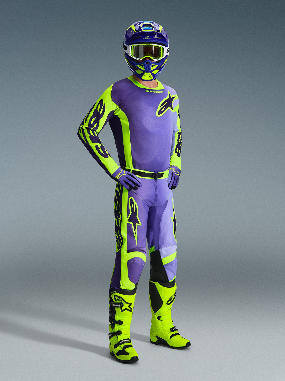 Pilote de motocross portant la tenue Alpinestars Racer Portl 2026, maillot et pantalon violet et jaune fluo, bottes jaune néon, gants violets et casque assorti, équipement complet coordonné pour la performance motocross tout-terrain