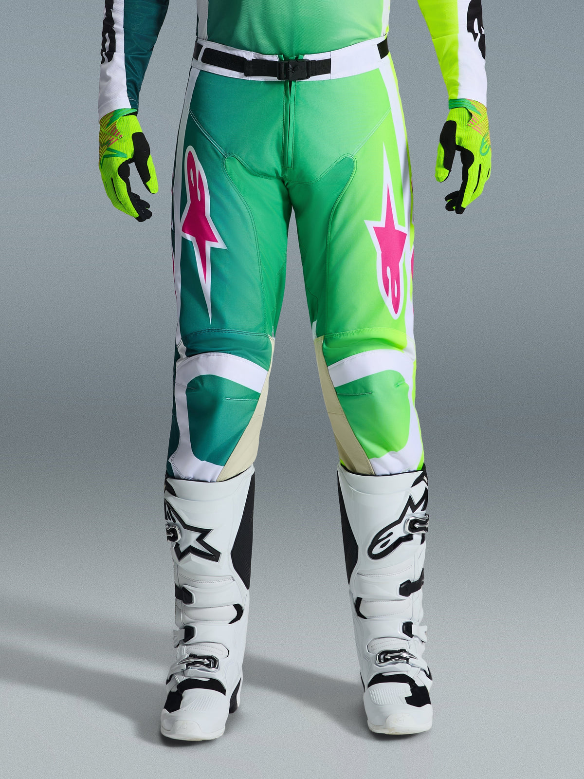Alpinestars 2026 Racer Portl Pants, pantalon de motocross, vert, blanc et noir avec logos d'étoiles roses, porté avec des bottes blanches et noires et des gants vert citron, doté d'un design en dégradé et d'une coupe ergonomique pour la course tout-terrain