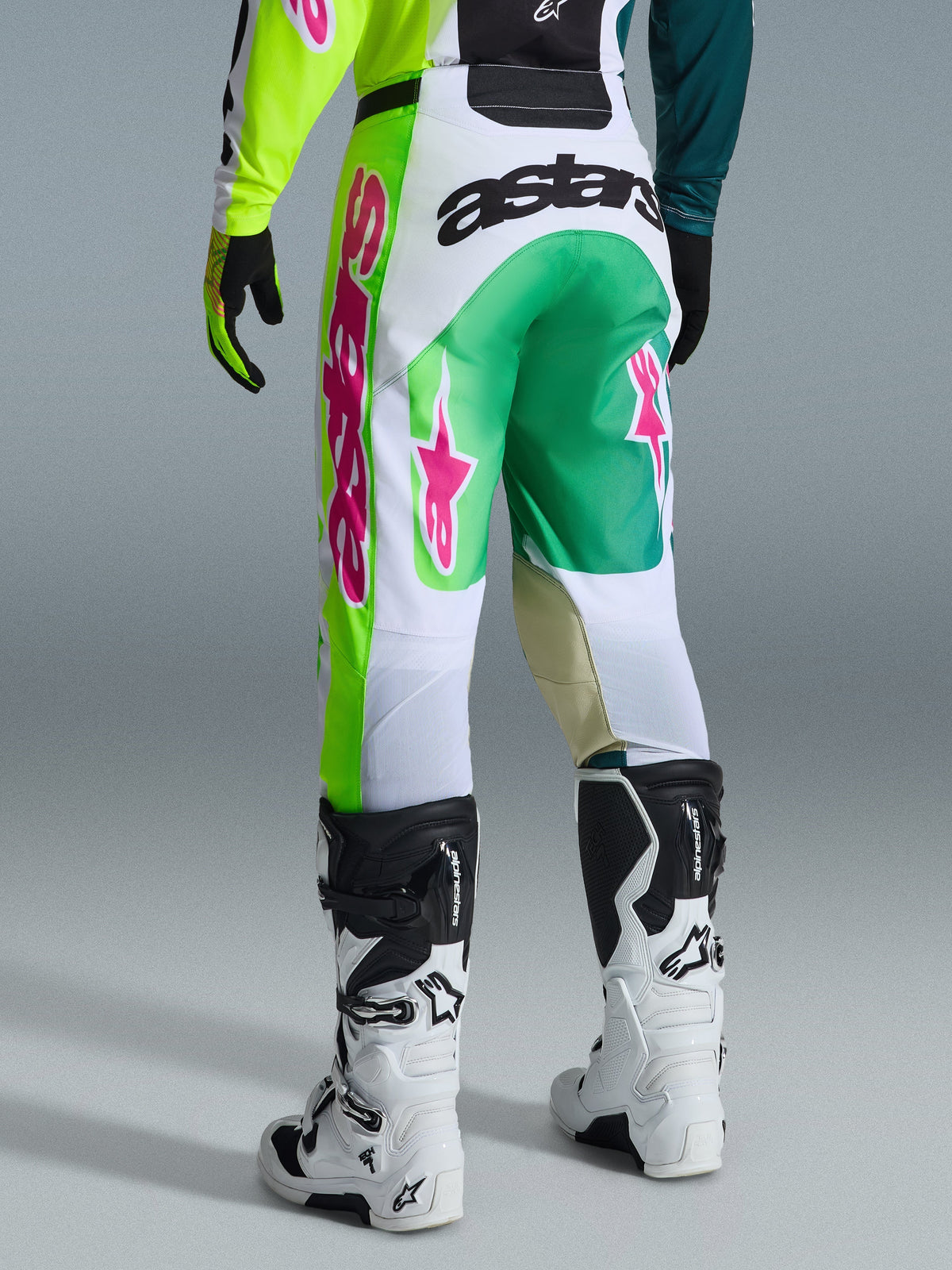 Pantalon Alpinestars Racer Portl 2026, pantalon de motocross, vert, blanc et noir avec des accents roses, vue arrière présentant le logo « astars » sur l'assise et des logos d'étoiles roses sur les jambes, associé à des bottes de motocross blanches et noires, équipement de performance pour la course tout-terrain
