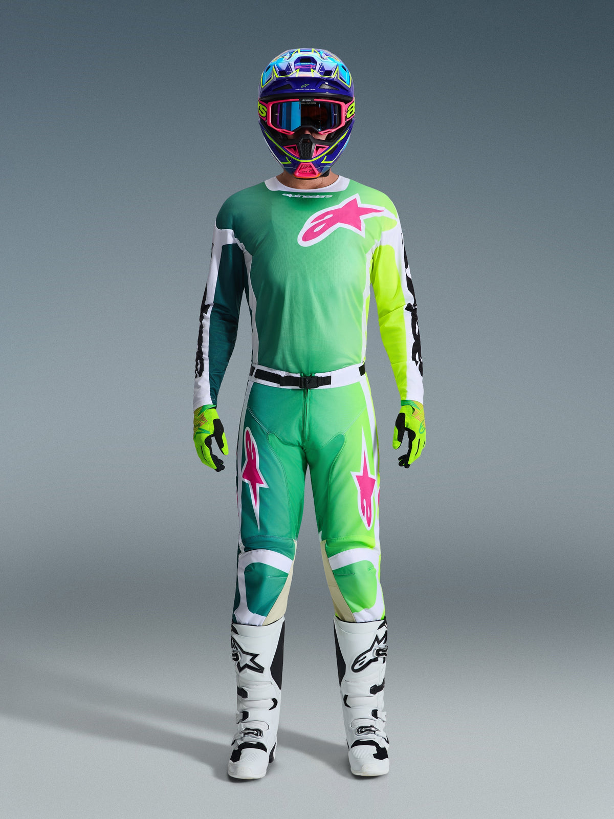 Pantalon Alpinestars 2026 Racer Portl, pantalon de motocross, vert, blanc et noir avec des accents de logo roses, porté dans le cadre d'un équipement de course complet avec un maillot assorti, des bottes blanches et un casque multicolore, tenue coordonnée pour la course tout-terrain professionnelle.