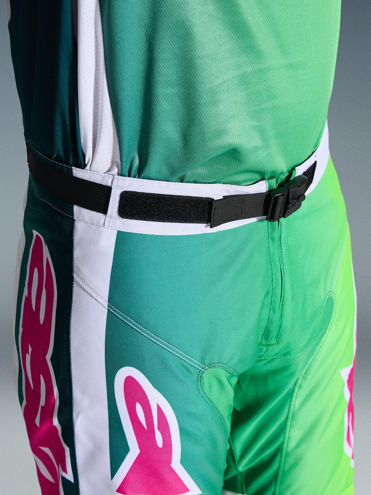 Pantalon Alpinestars Racer Portl 2026, pantalon de motocross, vert, blanc et noir avec accents roses sur le logo, gros plan de la taille montrant la boucle magnétique SX2 et la fermeture réglable, équipement durable pour la course tout-terrain