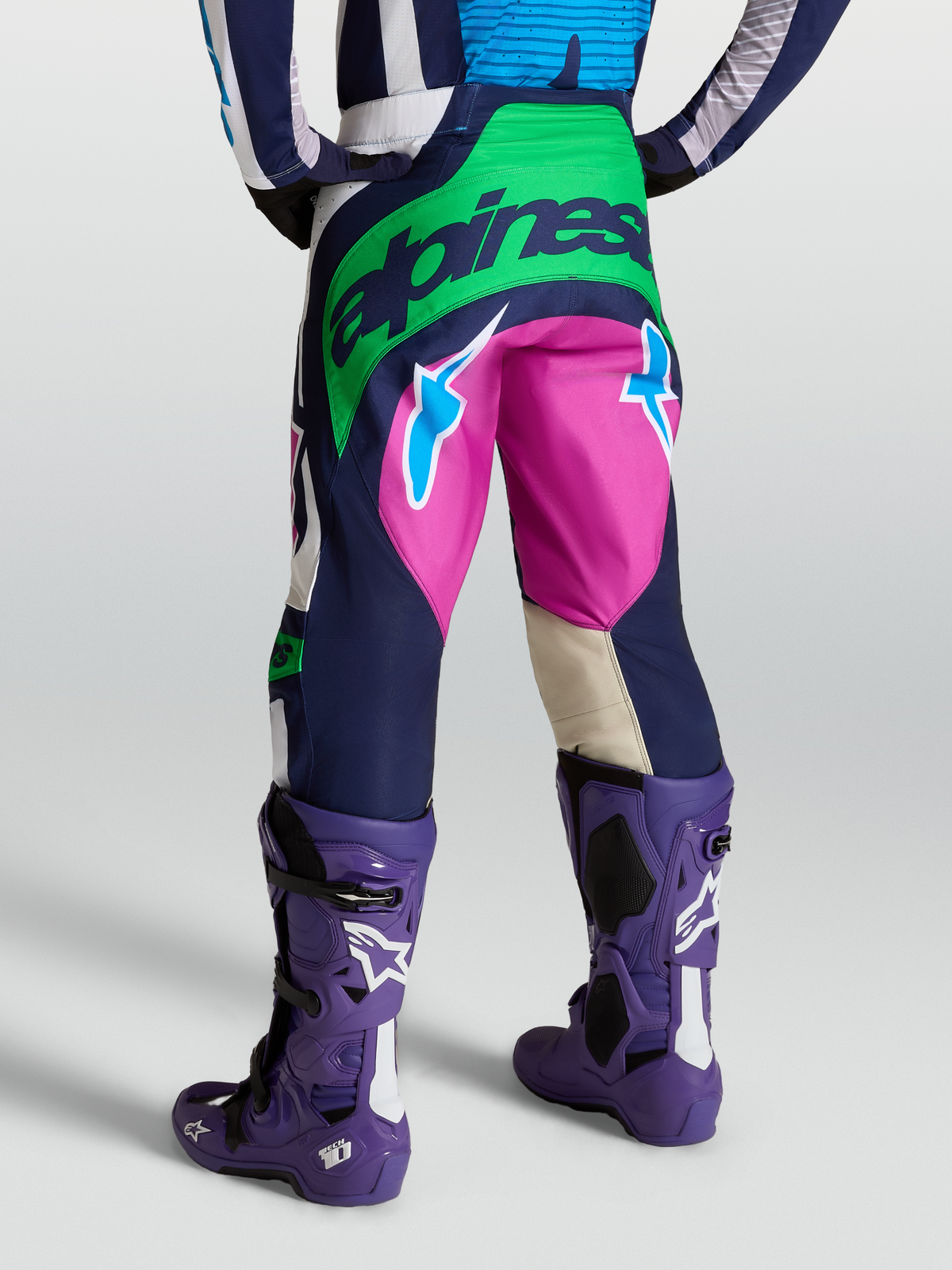 Alpinestars Pantalon Techstar Maven, équipement motocross bleu et vert, vue arrière avec bottes Tech 10 violettes.