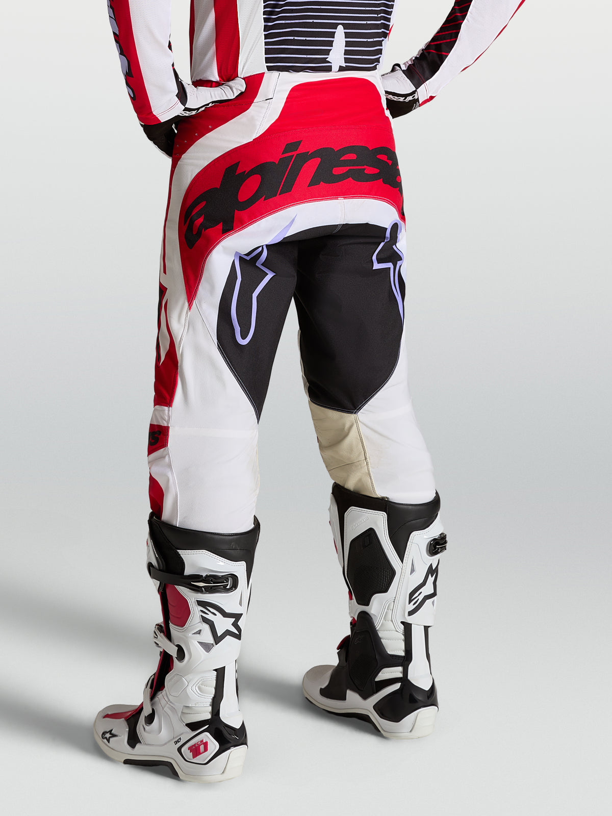 Alpinestars Techstar Maven, pantalon de motocross pour homme, rouge, blanc et noir, assise renforcée et coupe athlétique, vue de dos porté avec des bottes de moto