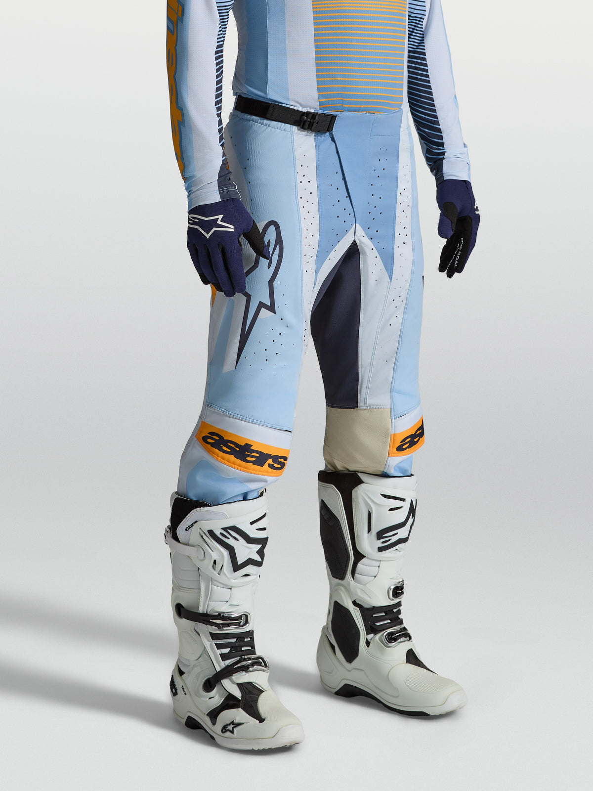Alpinestars Pantalon Techstar Maven, pantalon de motocross pour homme, bleu clair et orange, coupe de course ergonomique, porté par un pilote avec des bottes blanches, équipement de protection tout-terrain