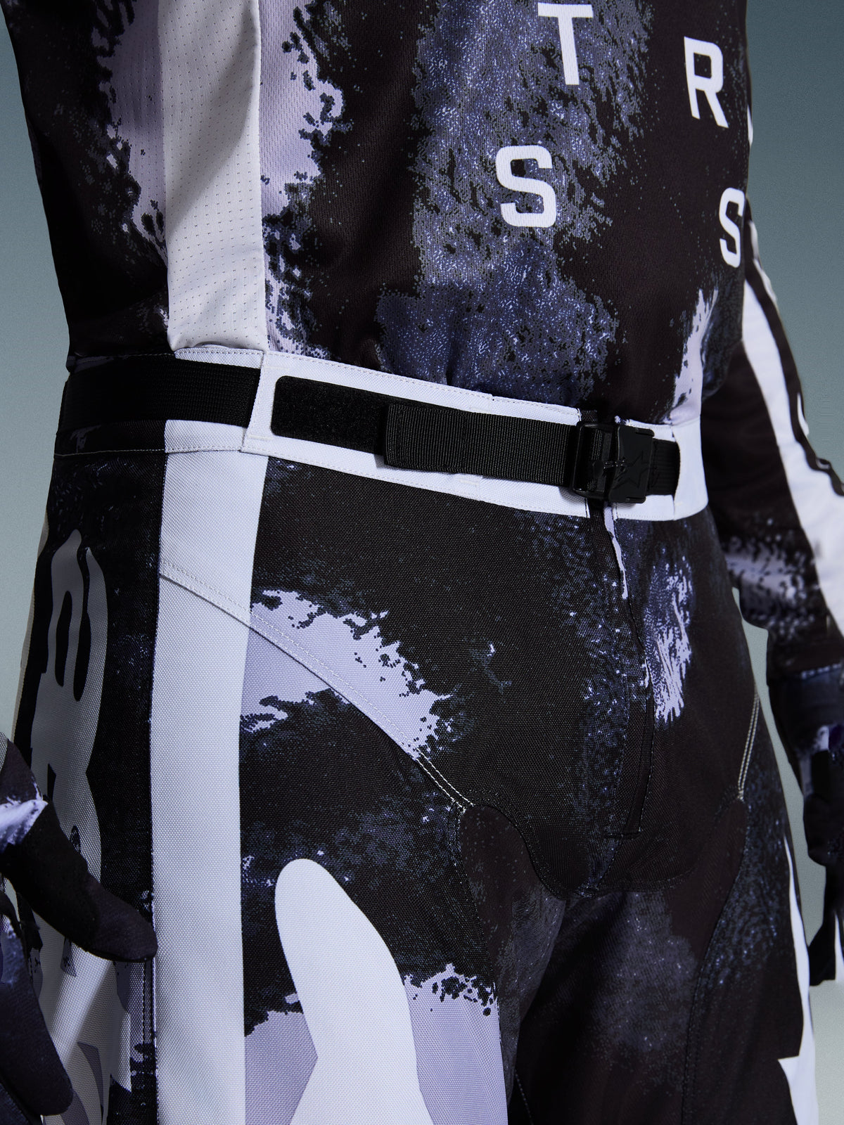 Pantalon Alpinestars Racer Lahnd 2026, pantalon de motocross Iron Camo, vue rapprochée de la ceinture réglable et de la boucle magnétique SX2, avec motif camouflage gris et noir et construction en poly-tissu 600D durable.
