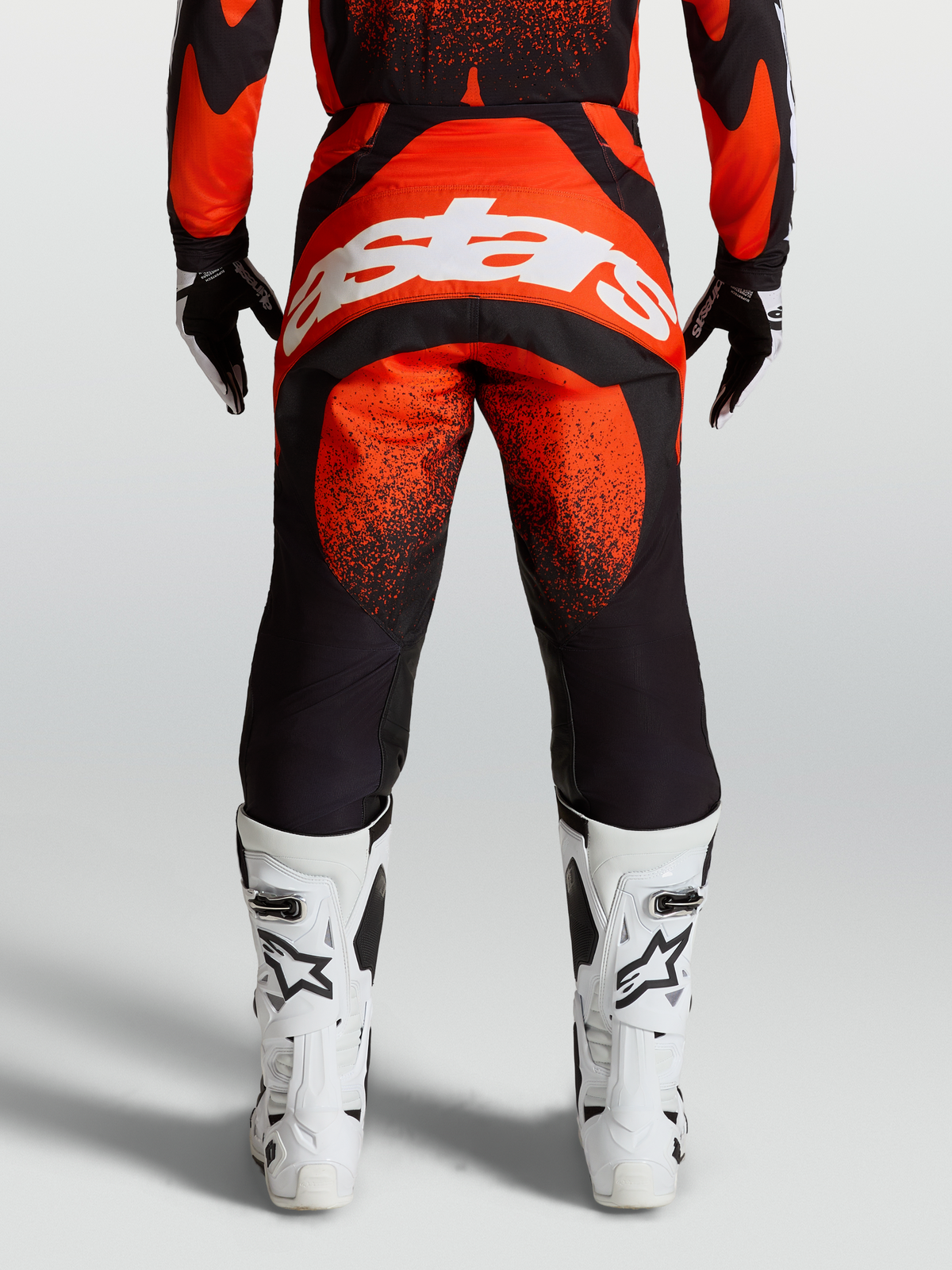 Alpinestars Pantalons Techstar Swan, équipement de motocross rouge et noir, vue de dos montrant le logo blanc et les bottes de course blanches.