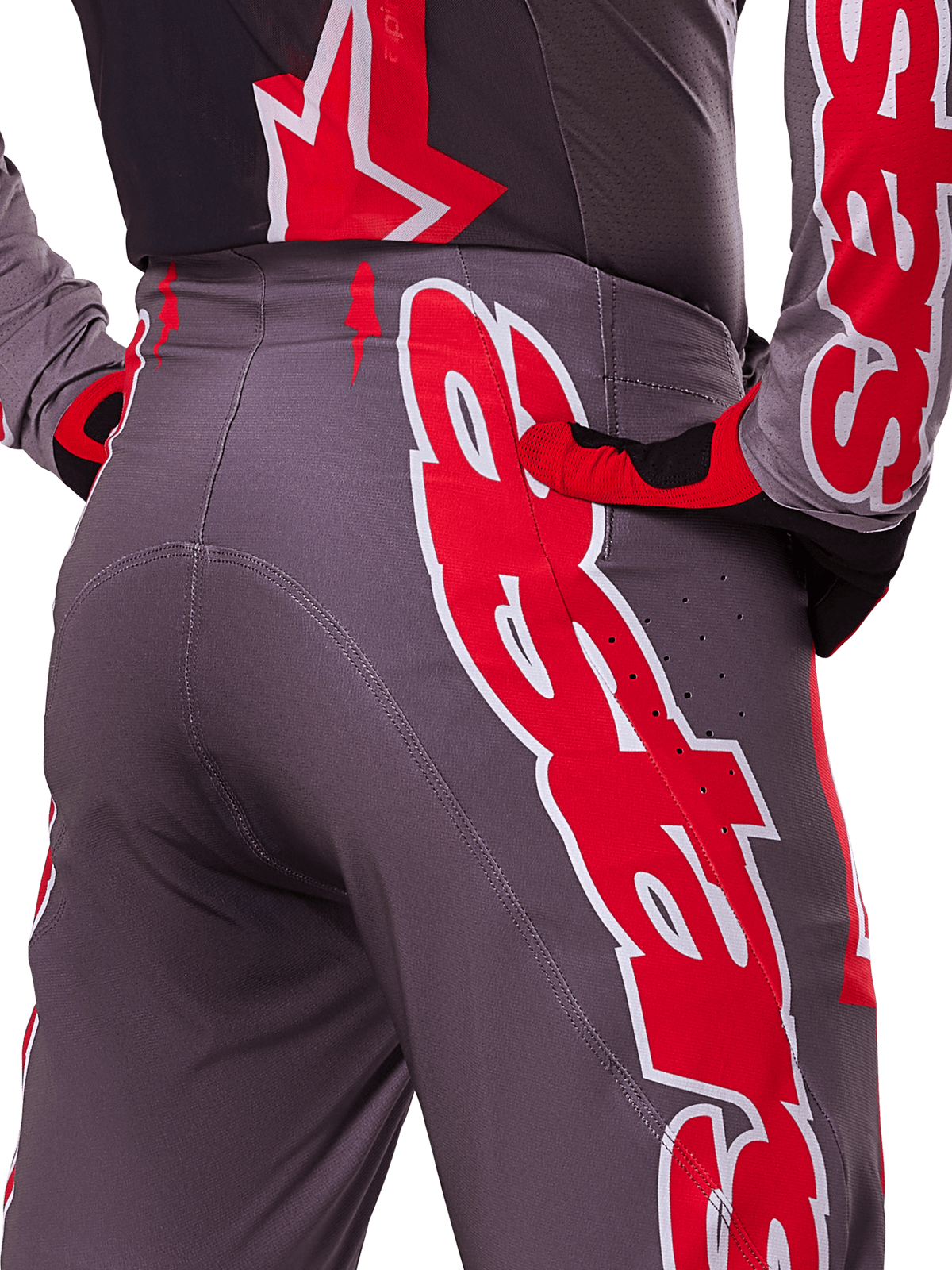 Alpinestars 2025 Supertech Lipan broek, motorcross broek, Smoke Bright Red en grijs, close-up van de heup en achterzijde met opvallende rode en witte logo's, ventilatieperforaties, atletische racepasvorm gedragen met bijpassende uitrusting.