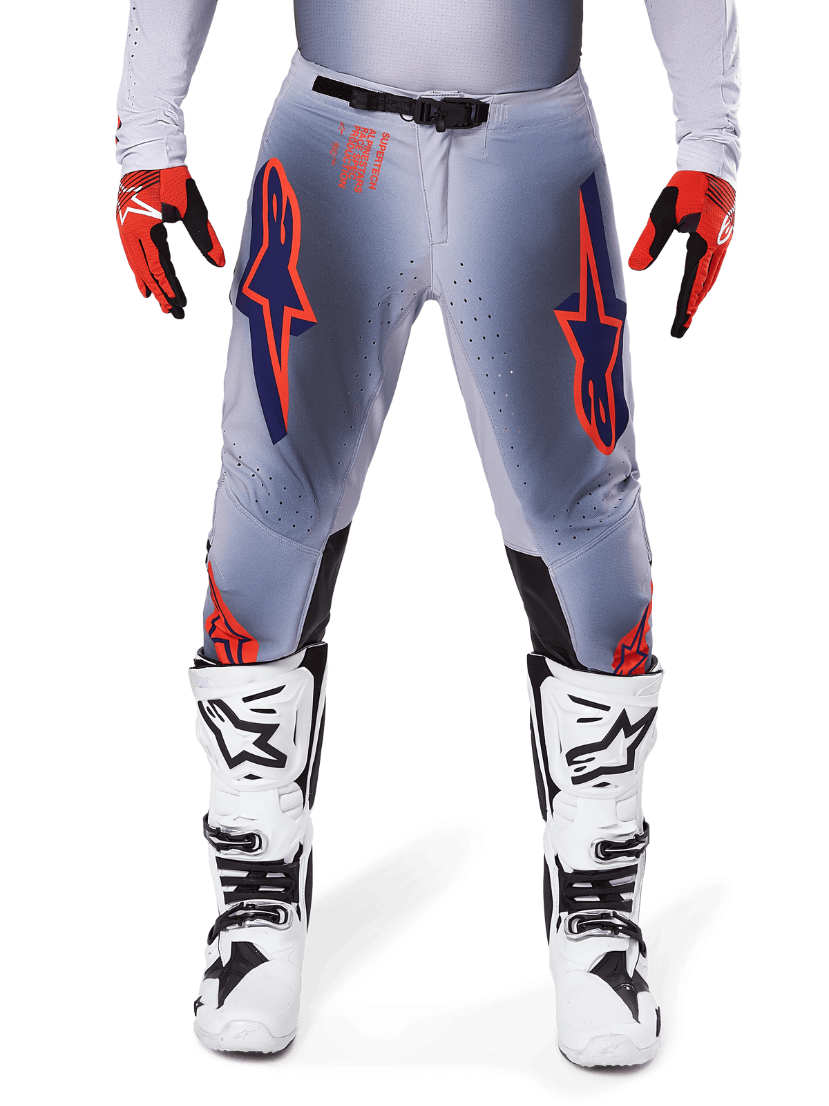 Alpinestars 2025 Supertech Lipan Hose, Motocross-Hose, Grau und Orange Fluo, getragen mit rot-schwarzen Handschuhen und weiß-schwarzen Stiefeln, mit großen Alpinestars Stern-Logos auf den Oberschenkeln und Belüftungsperforationen für Rennsport auf Profi-Niveau.