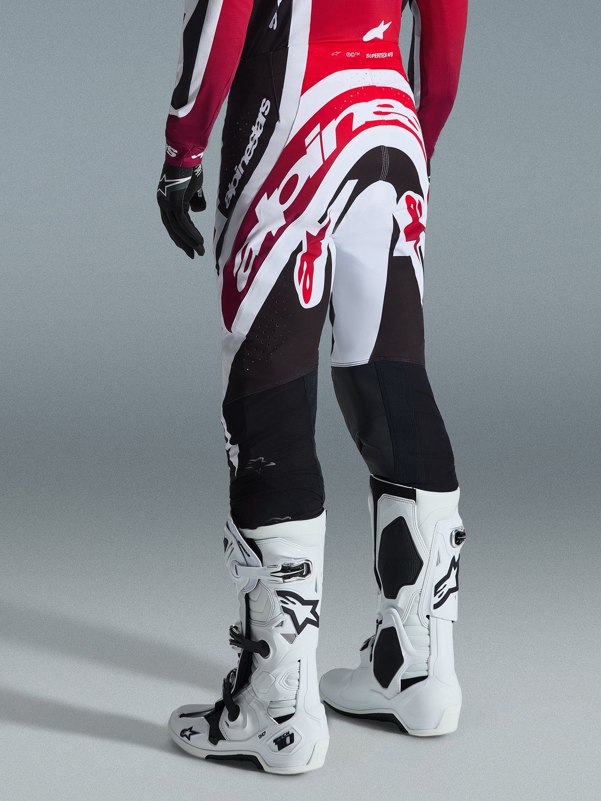 Alpinestars 2026 Supertech AFD Vista Pants, Motocross Pants, Black Red and White, rear view with large Alpinestars branding on the seat, paired with white Tech 10 boots and black gloves, athletic design for elite off-road performance