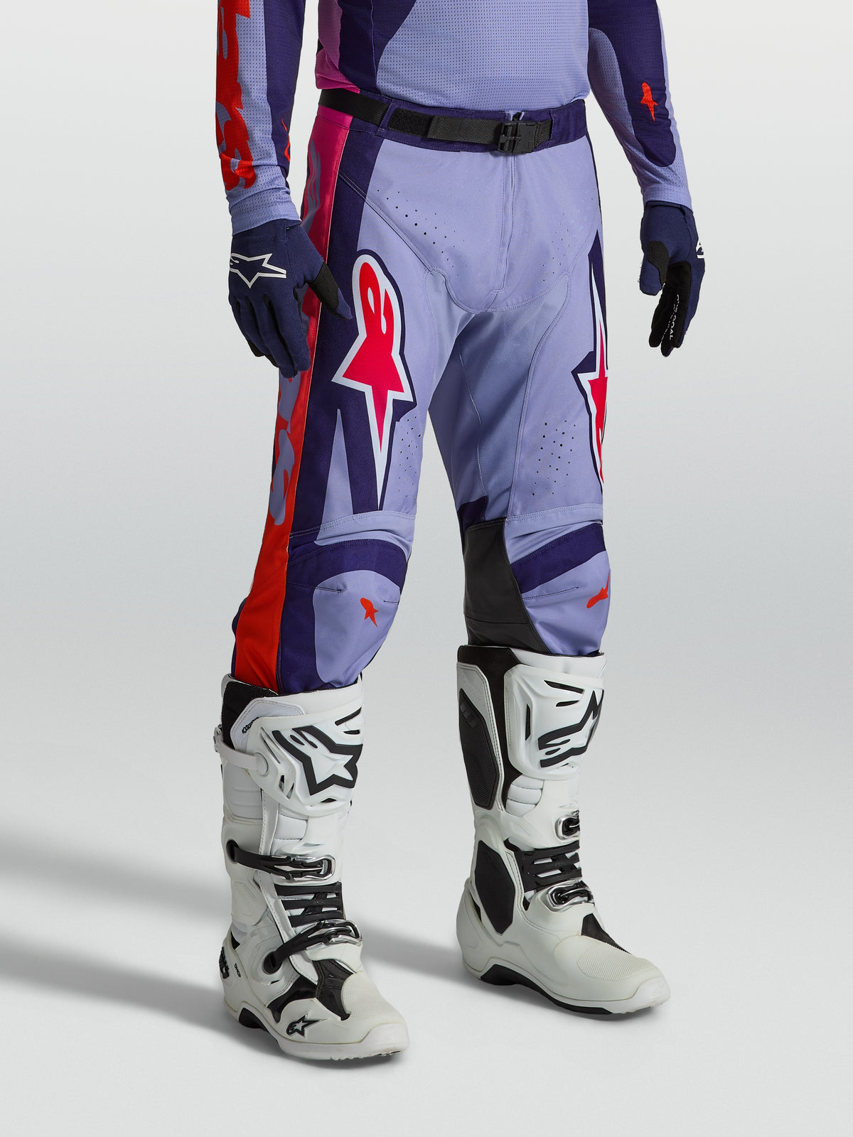 Alpinestars pantalons Racer Air Hunt, équipement de motocross ventilé violet et rose, porté avec des bottes de moto blanches.