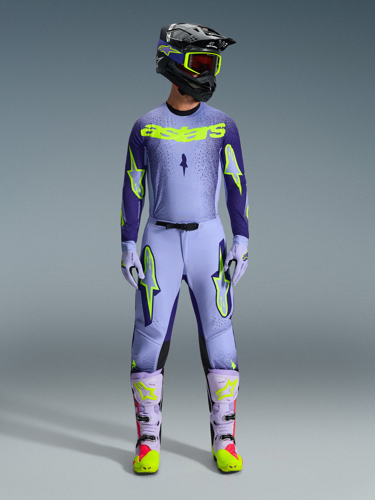 Alpinestars 2026 Supertech Scenz broek, motorcross broek, Purple Yellow Fluo, gedragen als een complete race-uitrusting met bijpassende lavendel jersey, handschoenen en laarzen, voorzien van opvallende geel fluo logo's, atletische pasvorm voor professionele off-road racing.