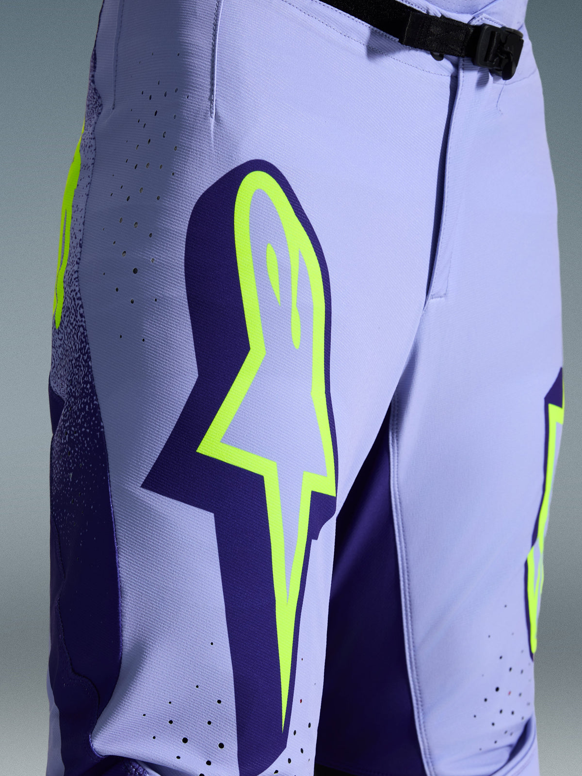 Alpinestars 2026 Supertech Scenz crossbroek, motorcross broek, paars met fluogeel, close-up met groot geel logo op de dij, lasergesneden perforaties voor ventilatie en magnetische gesp bij de taille, sportieve off-road uitrusting