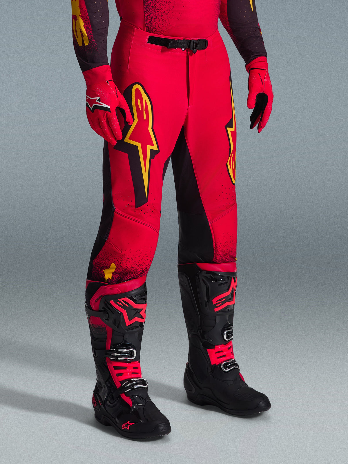 Alpinestars 2026 Supertech Scenz Pants, pantalon de motocross, rouge, noir et jaune, avec des logos Alpinestars jaunes et des empiècements noirs, porté avec un maillot rouge assorti, des gants rouges et des bottes de motocross noires.