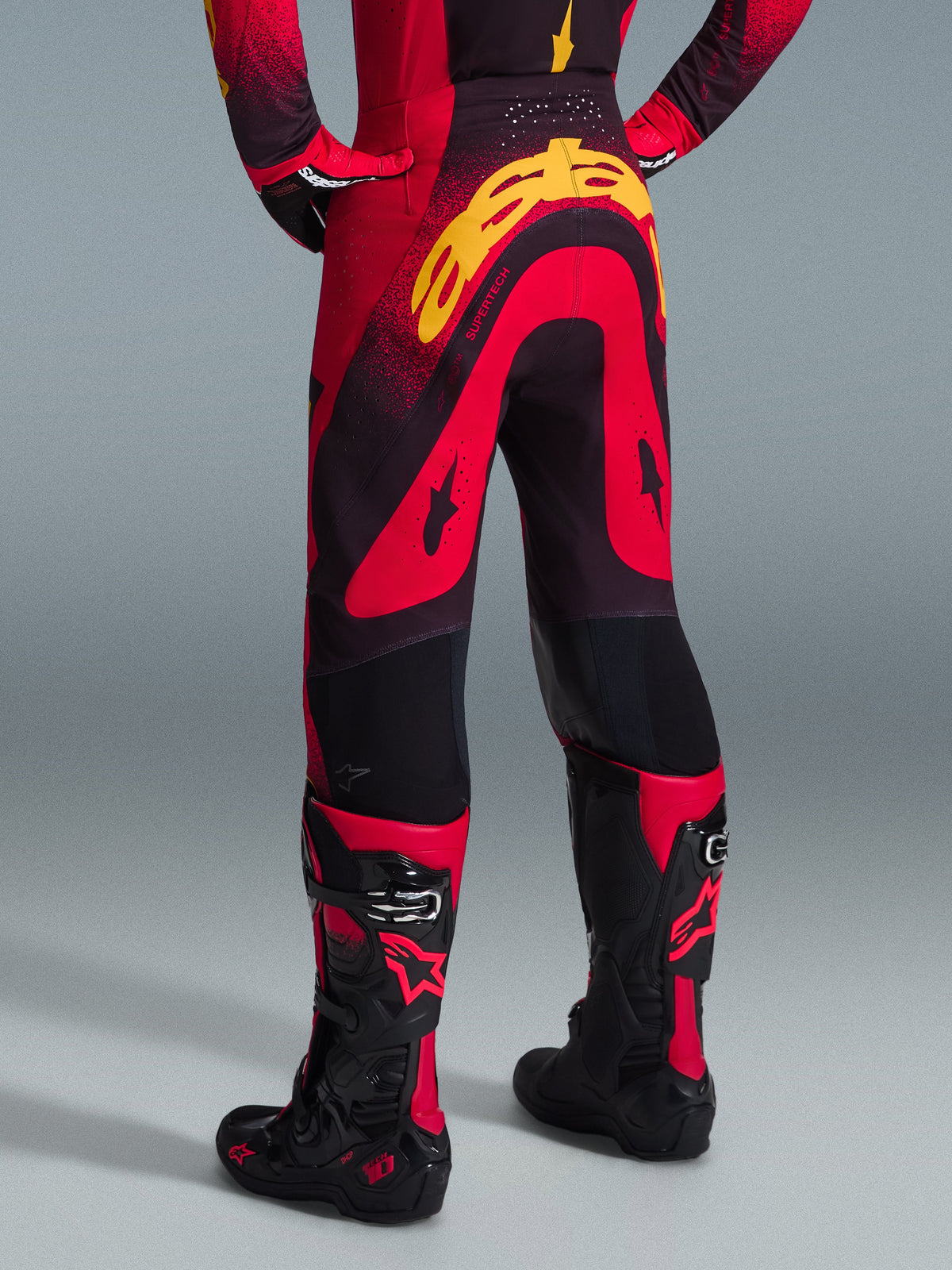 Alpinestars 2026 Supertech Scenz Pants, pantalon de motocross, rouge, noir et jaune, vue arrière montrant un grand marquage Alpinestars jaune sur l'assise, porté avec un maillot assorti et des bottes de motocross rouges et noires.