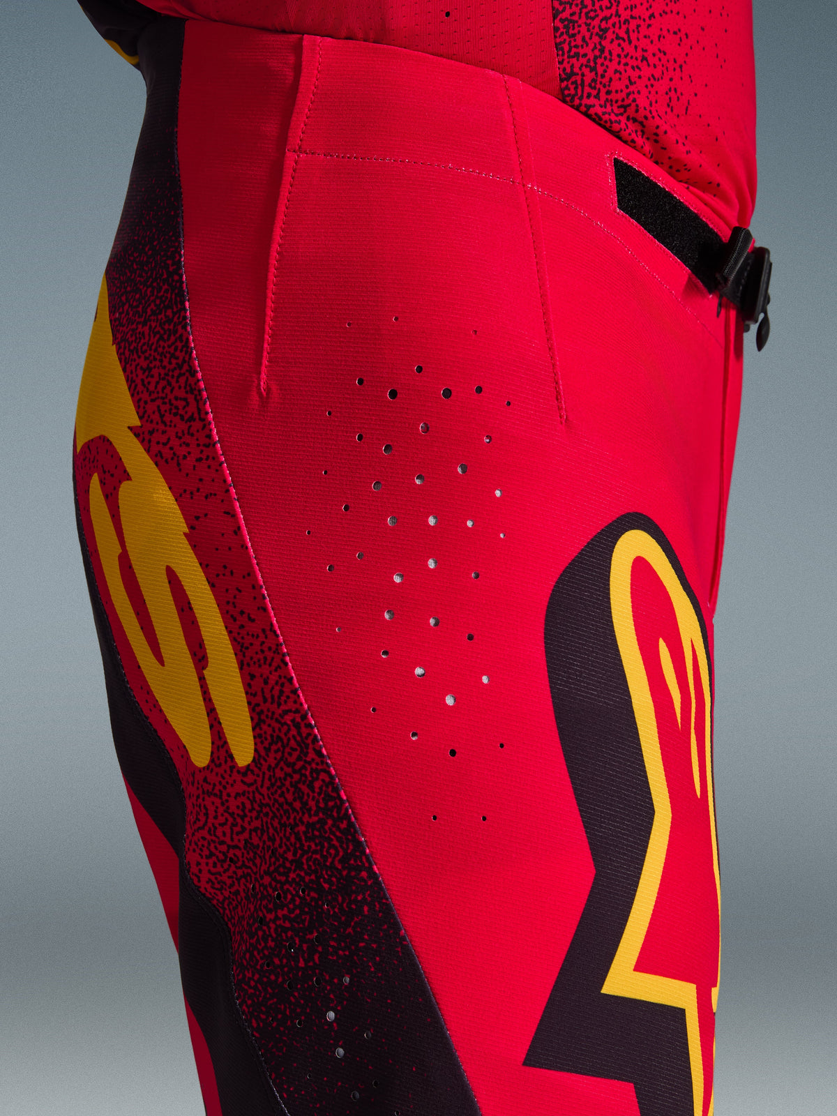 Pantalon Alpinestars Supertech Scenz 2026, pantalon de motocross, rouge, noir et jaune, vue latérale rapprochée montrant les perforations de ventilation découpées au laser, les logos graphiques audacieux et le tissu rip-stop extensible haute performance pour la course de motocross.