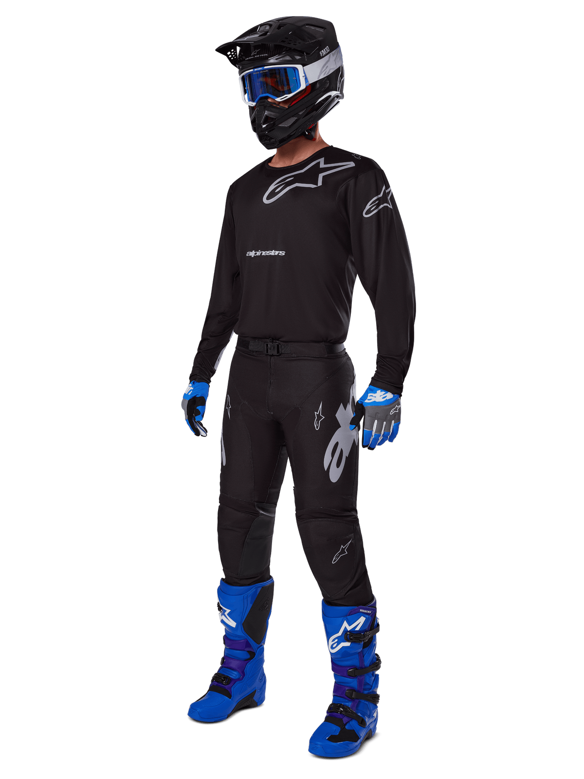 Motocross-Fahrer in kompletter Alpinestars-Rennausrüstung, 2025 Racer Graphite Hose in Schwarz und Grau, passendes schwarzes Trikot mit grauen Logos, schwarzer Helm mit blauer Brille, leuchtend blaue und violette Stiefel, blau-graue Handschuhe, koordiniertes Outfit für den Offroad-Rennsport