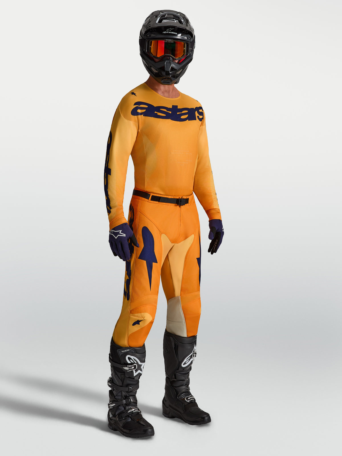Alpinestars Racer Amber, pantalon et maillot de motocross pour homme, orange et bleu foncé, avec bottes et casque noirs, équipement tout-terrain de performance.