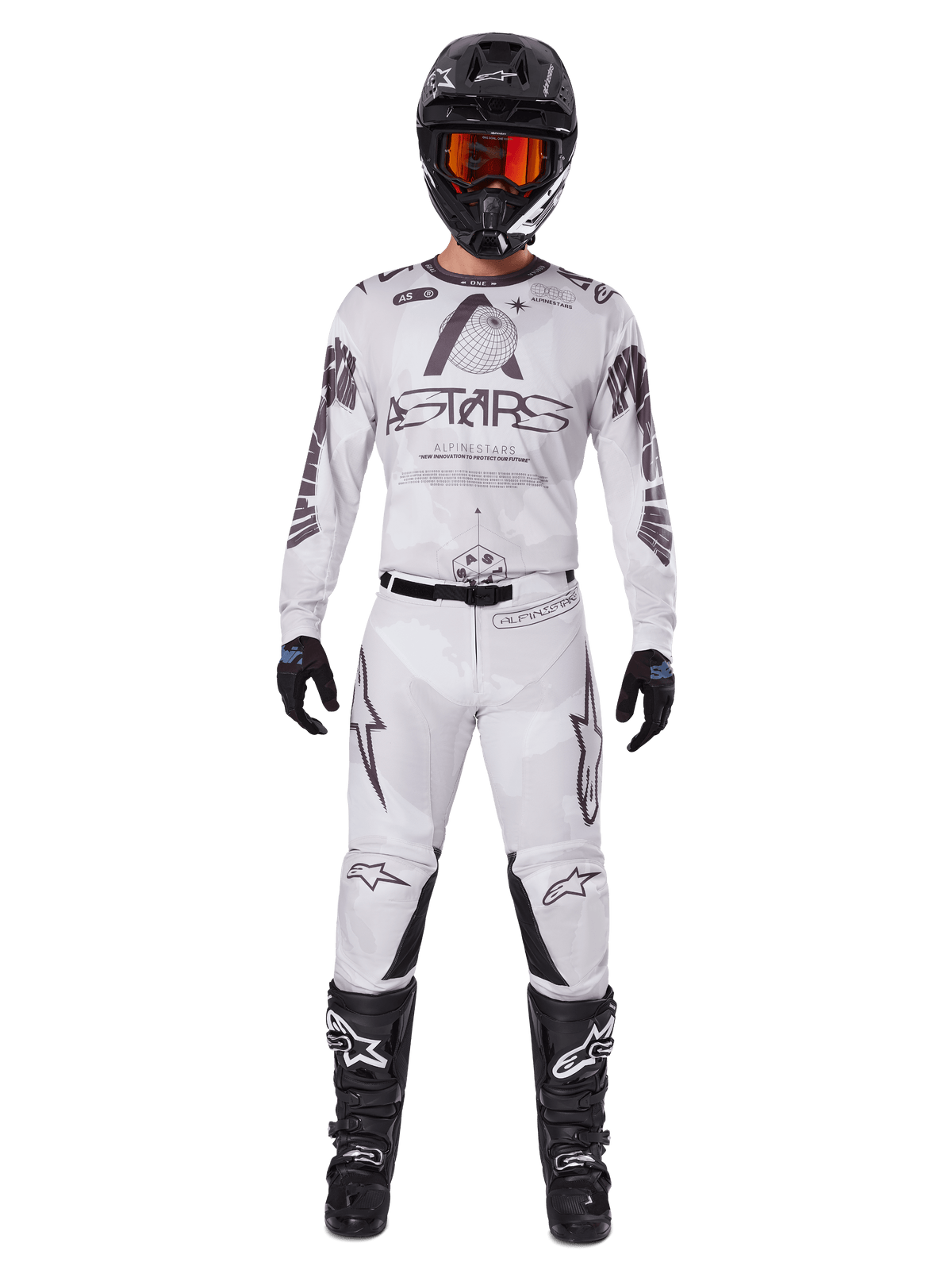 Motorcrossrijder in Alpinestars 2025 Racer Hollow crossbroek in Light Camo Brown, gecombineerd met een bijpassend wit en grijs shirt met lange mouwen, zwarte helm met oranjerode bril, zwarte handschoenen en zwarte laarzen, gecoördineerde race-uitrusting voor off-road prestaties.
