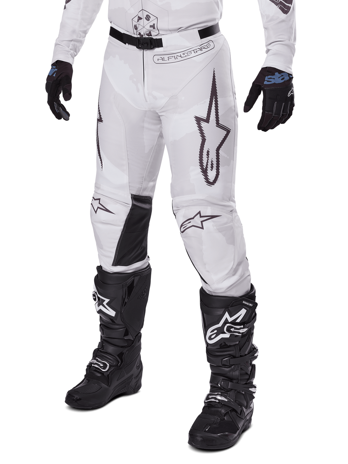 Alpinestars 2025 Racer Hollow Pants, motorcross broek, wit en grijs camo, met grote zwart omijnde sterlogo's en zwarte leren binnenkniepanelen, gedragen met zwarte motorcrosslaarzen en handschoenen, duurzaam ontwerp voor terreinrijden